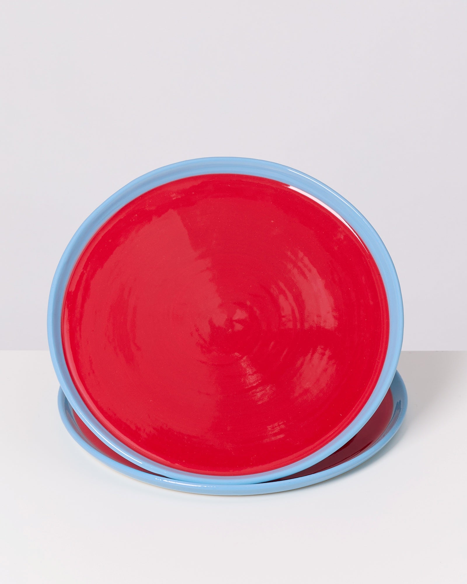 Zwei runde, rote Teller mit blauem Rand stehen auf einem weißen Hintergrund.