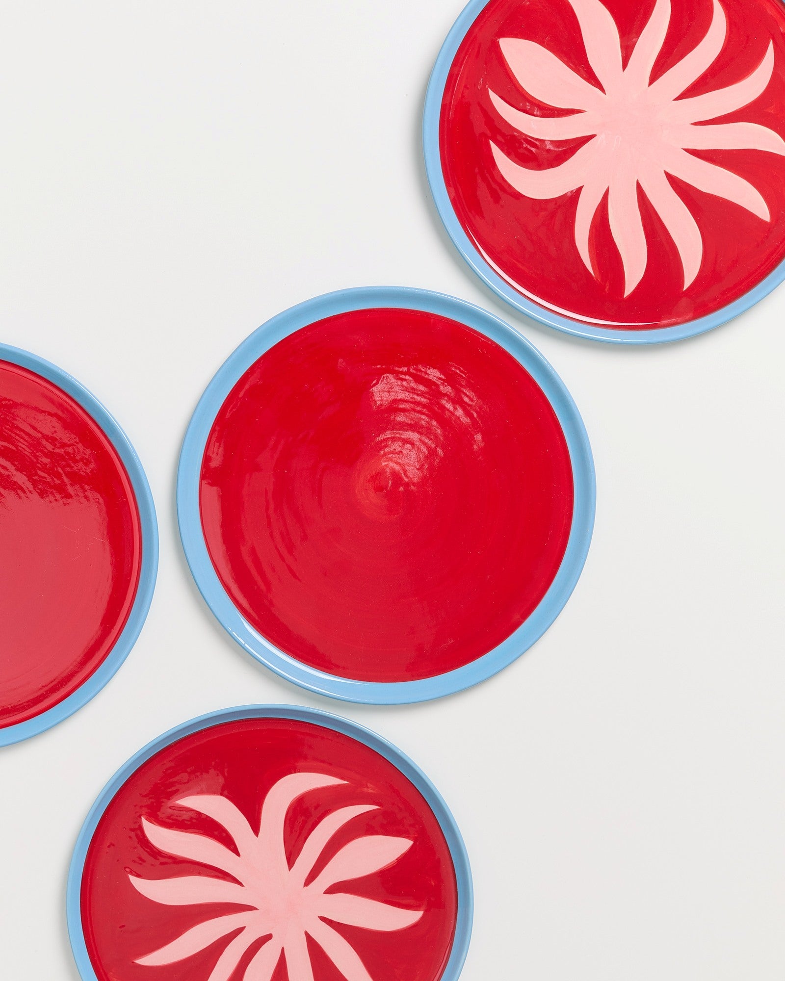 Vier rote Teller mit blauem Rand auf weißem Hintergrund, zwei haben ein pinkes Blumenmuster.