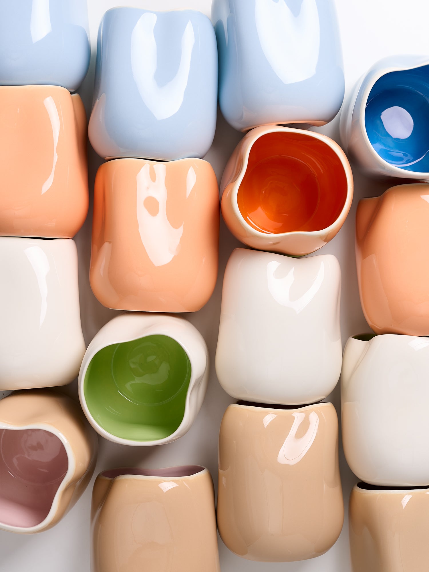 Bunte, unregelmäßig geformte Keramikgefäße in Pastelltönen mit glänzender Oberfläche, im Raster angeordnet.