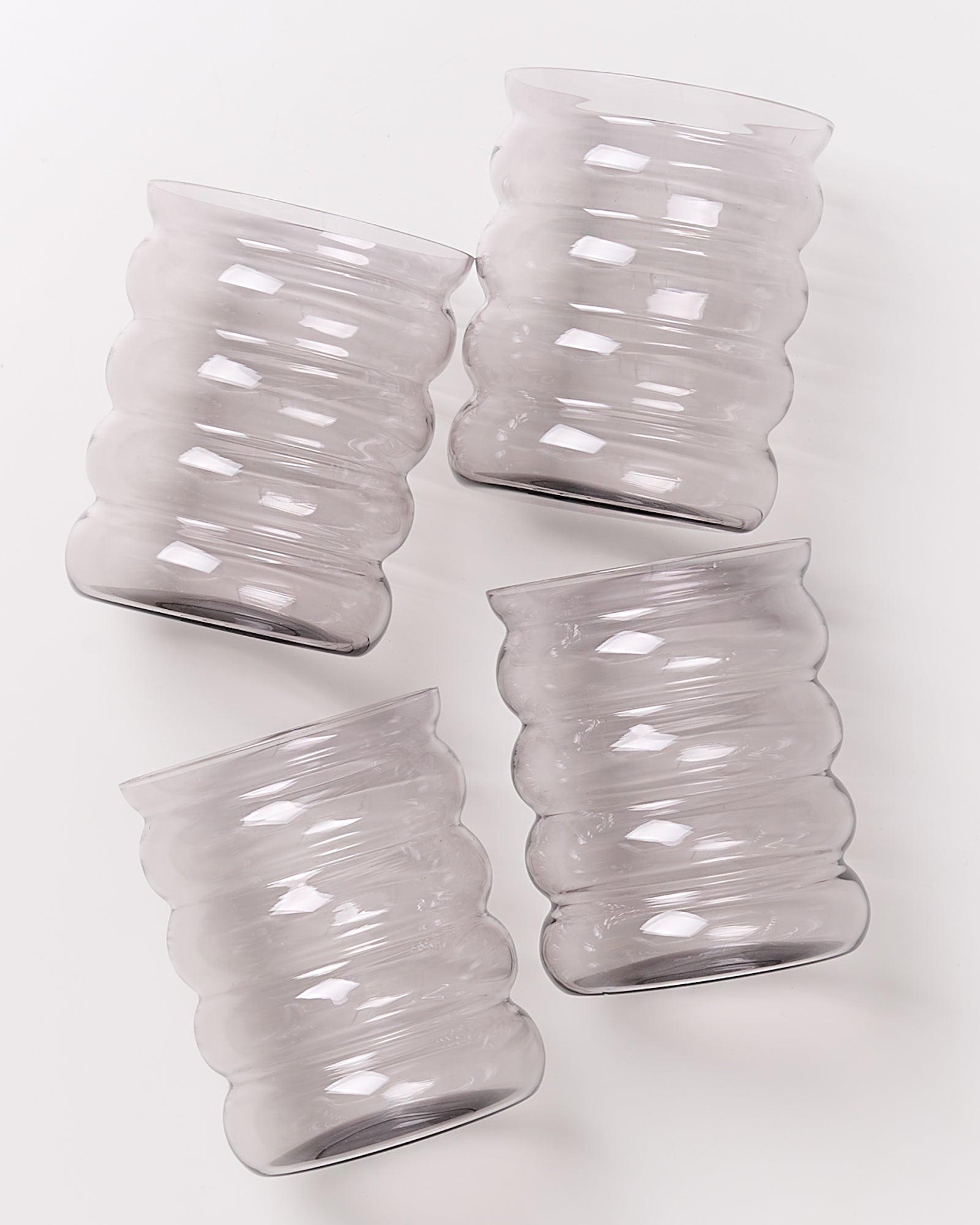 Vier gerippte Gläser aus transparentem Material liegen schräg auf einer weißen Oberfläche.