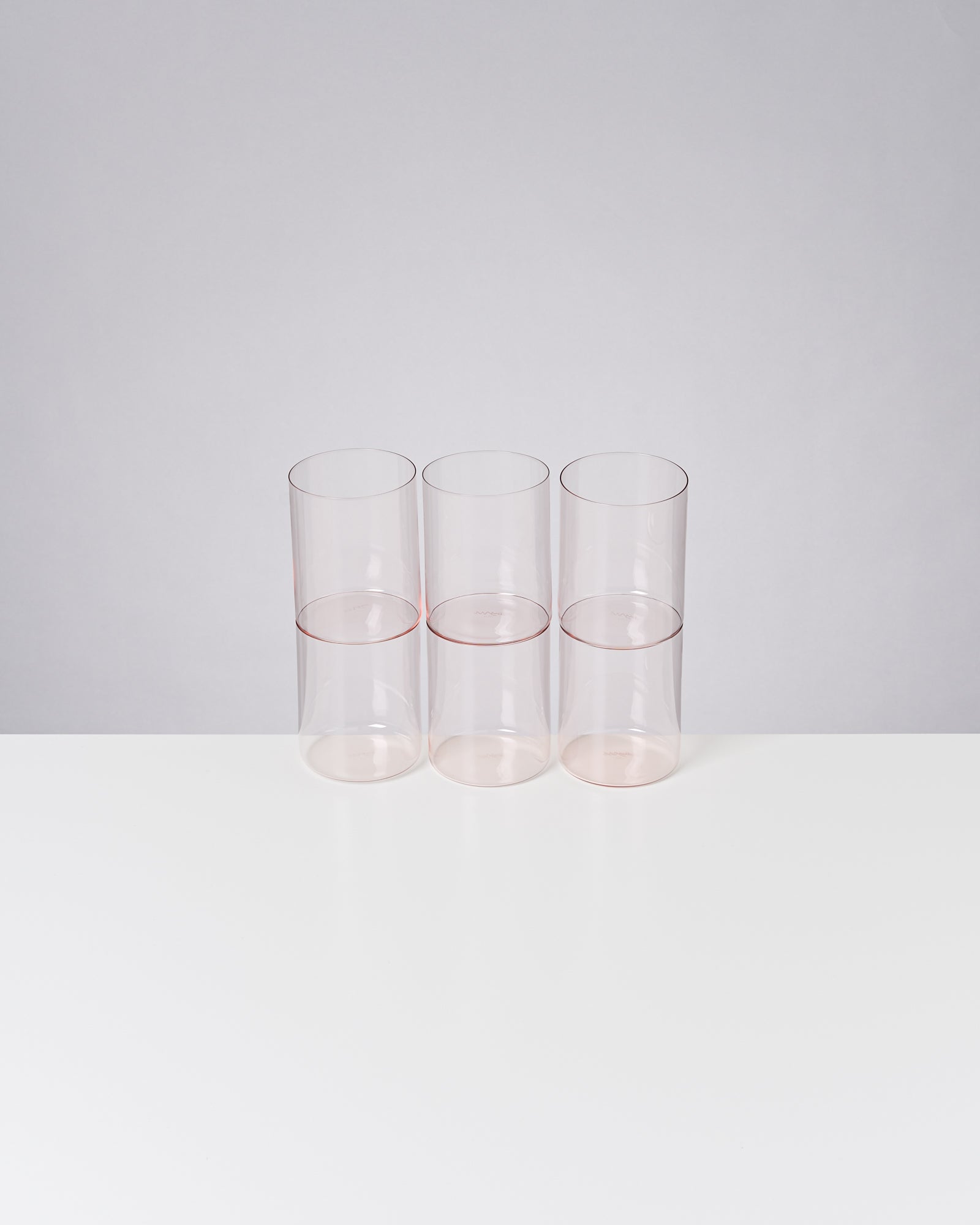 Drei nebeneinander stehende durchsichtige Gläser mit leicht rosafarbenem Rand auf einem weißen Hintergrund.