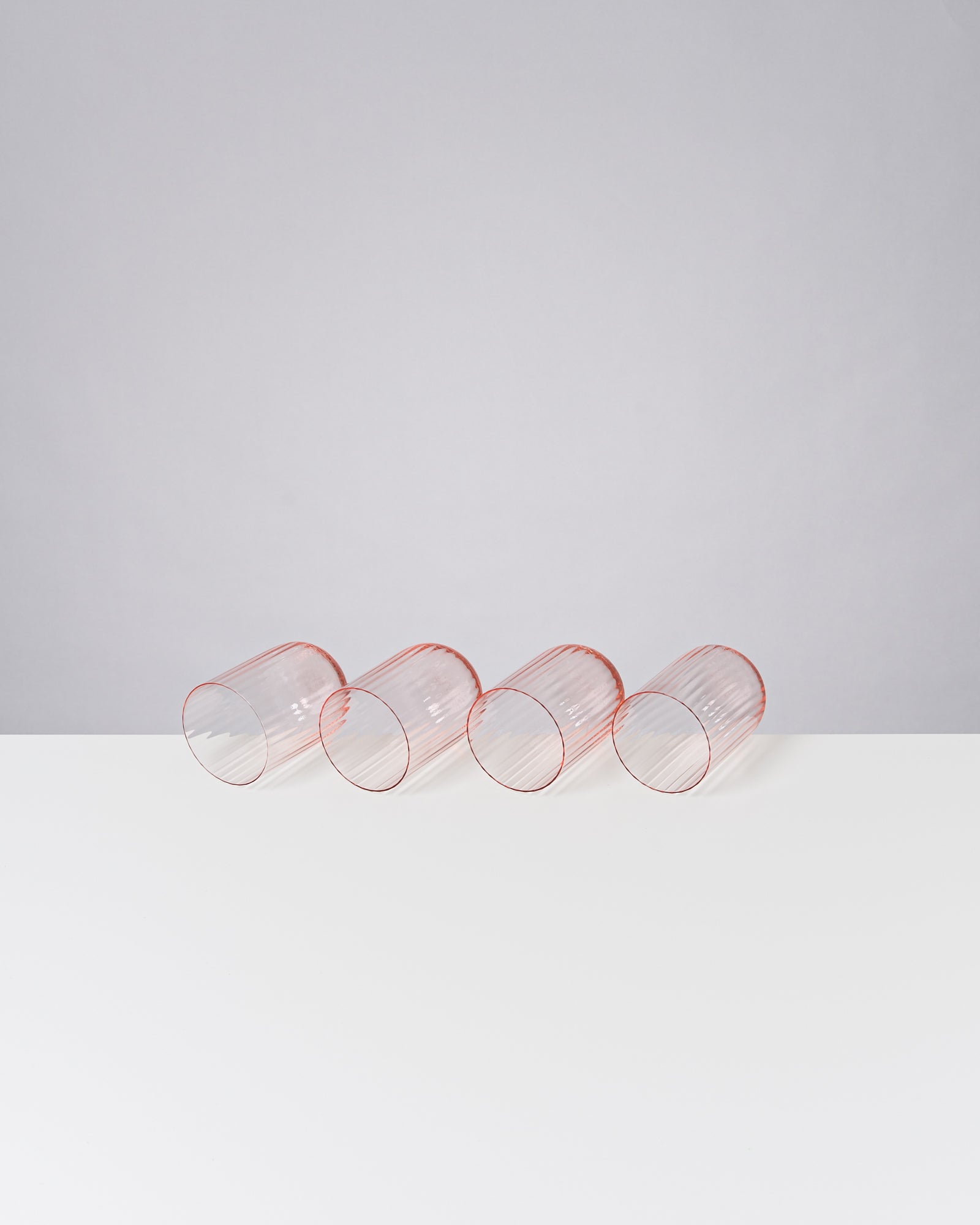 Vier liegende, durchsichtige rote Gläser auf einem weißen Tisch vor grauem Hintergrund.