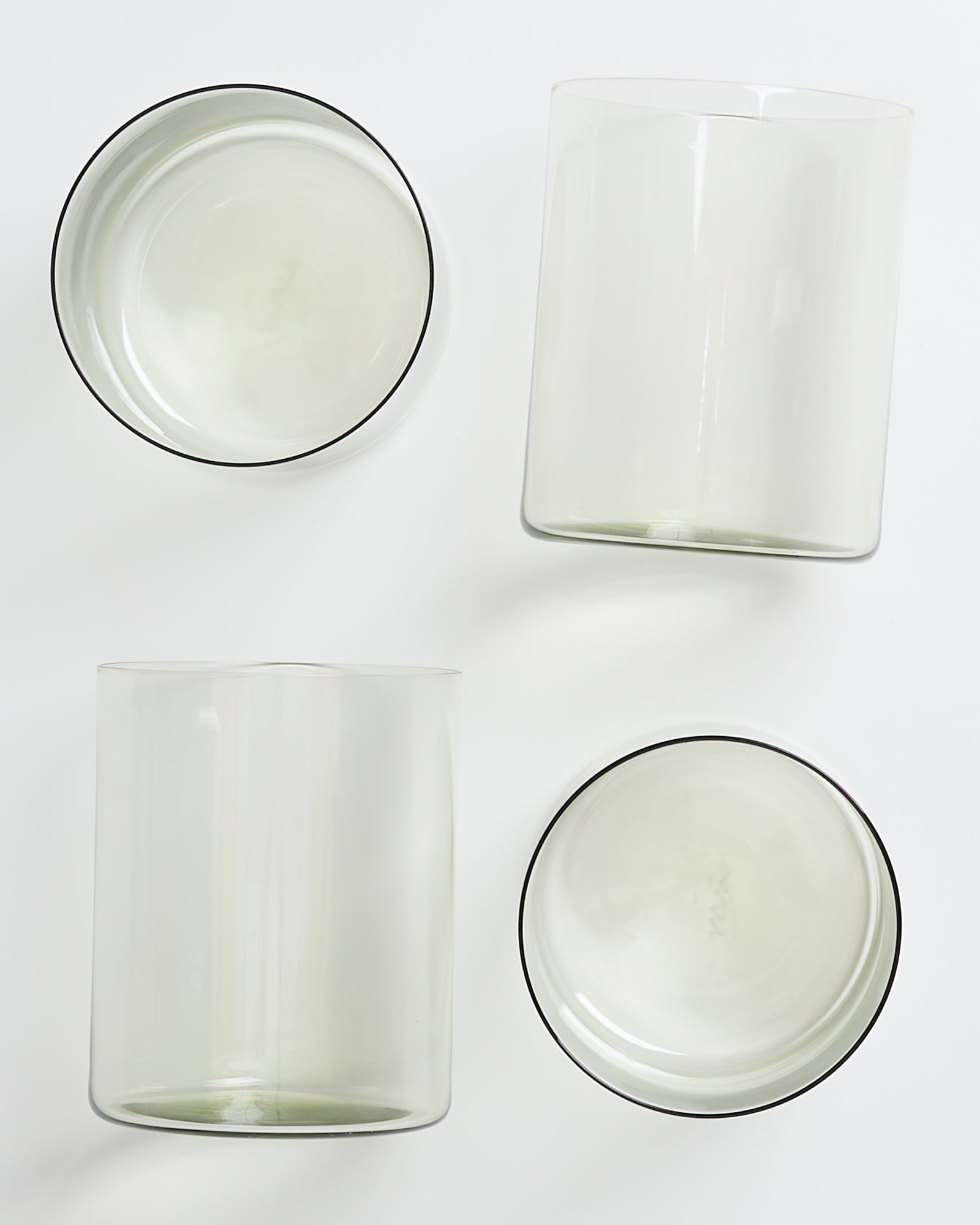 Vier leere, transparente Gläser in minimalistischem Design auf einer weißen Oberfläche.