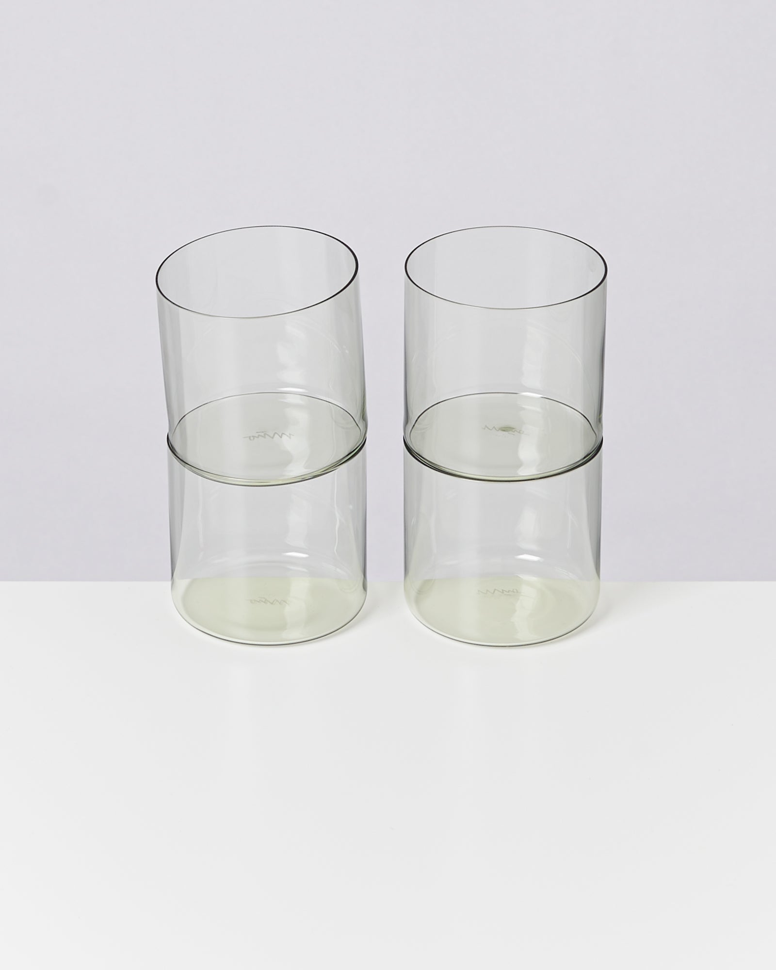 Zwei transparente Gläser stehen übereinander gestapelt auf einer weißen Oberfläche.