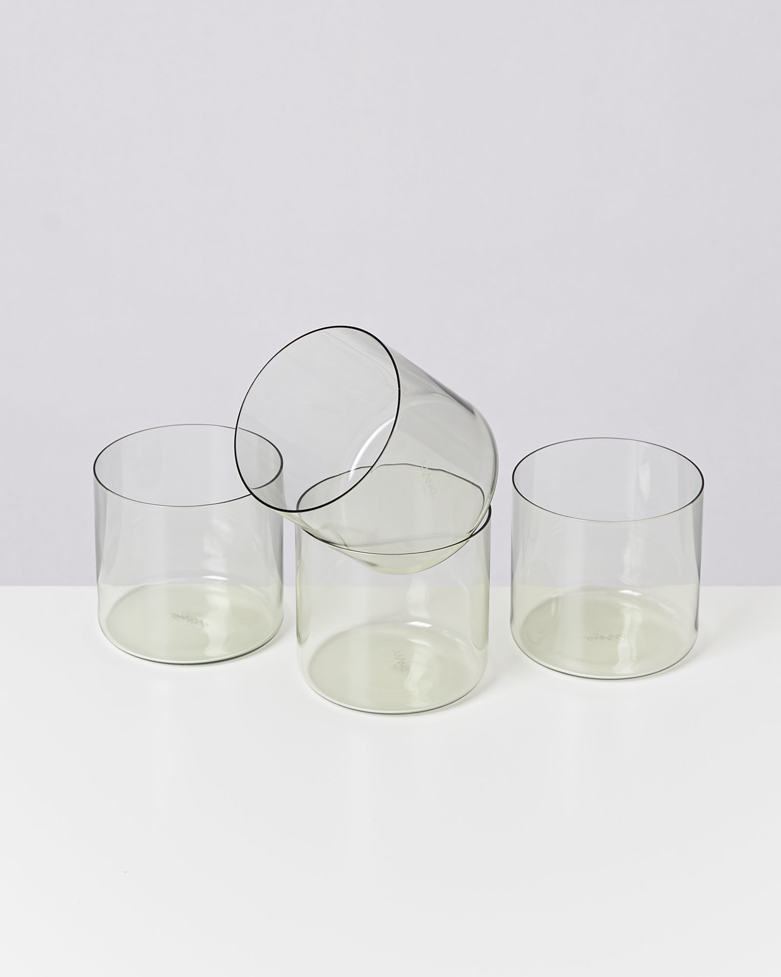 Vier durchsichtige Glasbecher auf einem weißen Hintergrund, einer liegt umgekippt auf den anderen.