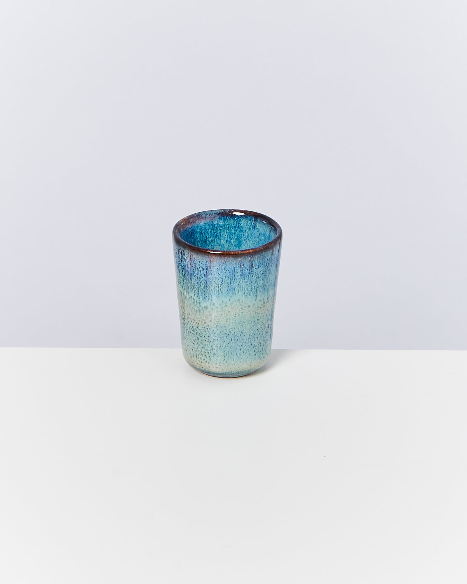 Ein blauer Keramikbecher mit Farbverlauf steht auf einem weißen Tisch vor neutralem Hintergrund.