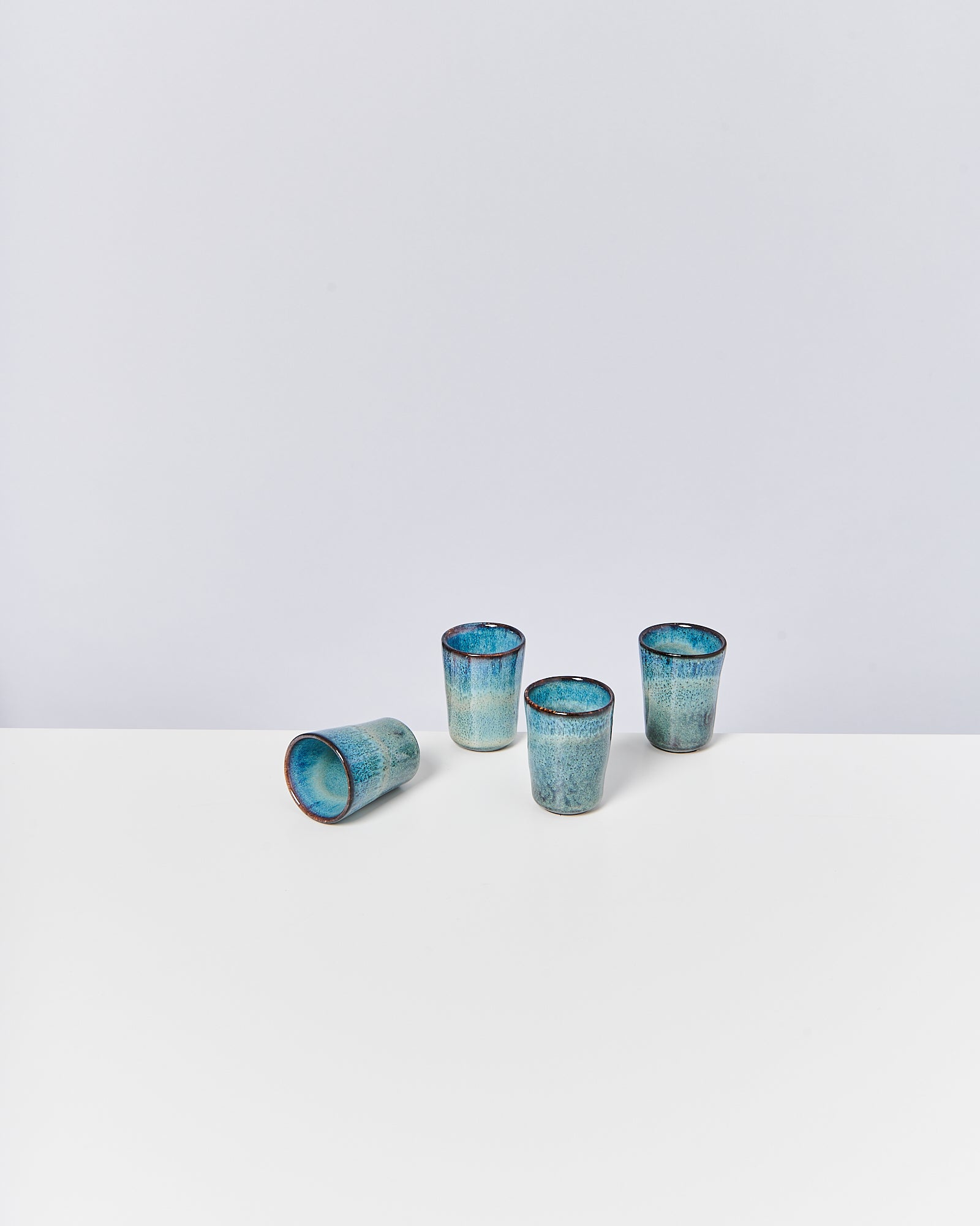 Vier blaue Becher aus Keramik stehen auf einem weißen Tisch, einer liegt auf der Seite.