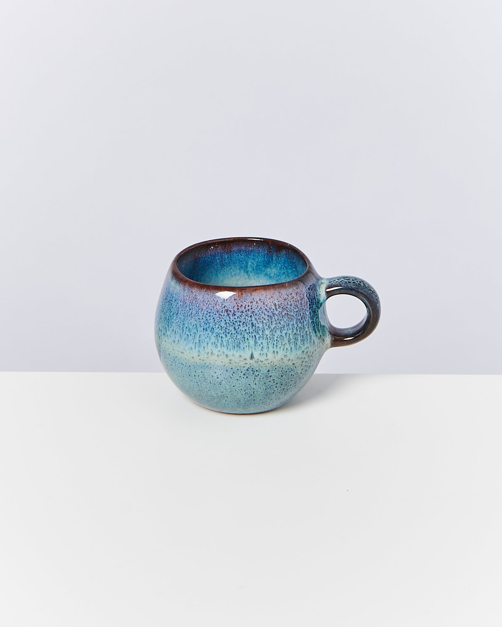 Keramiktasse in Blau- und Brauntönen mit Verlauf und rundem Henkel vor weißem Hintergrund.