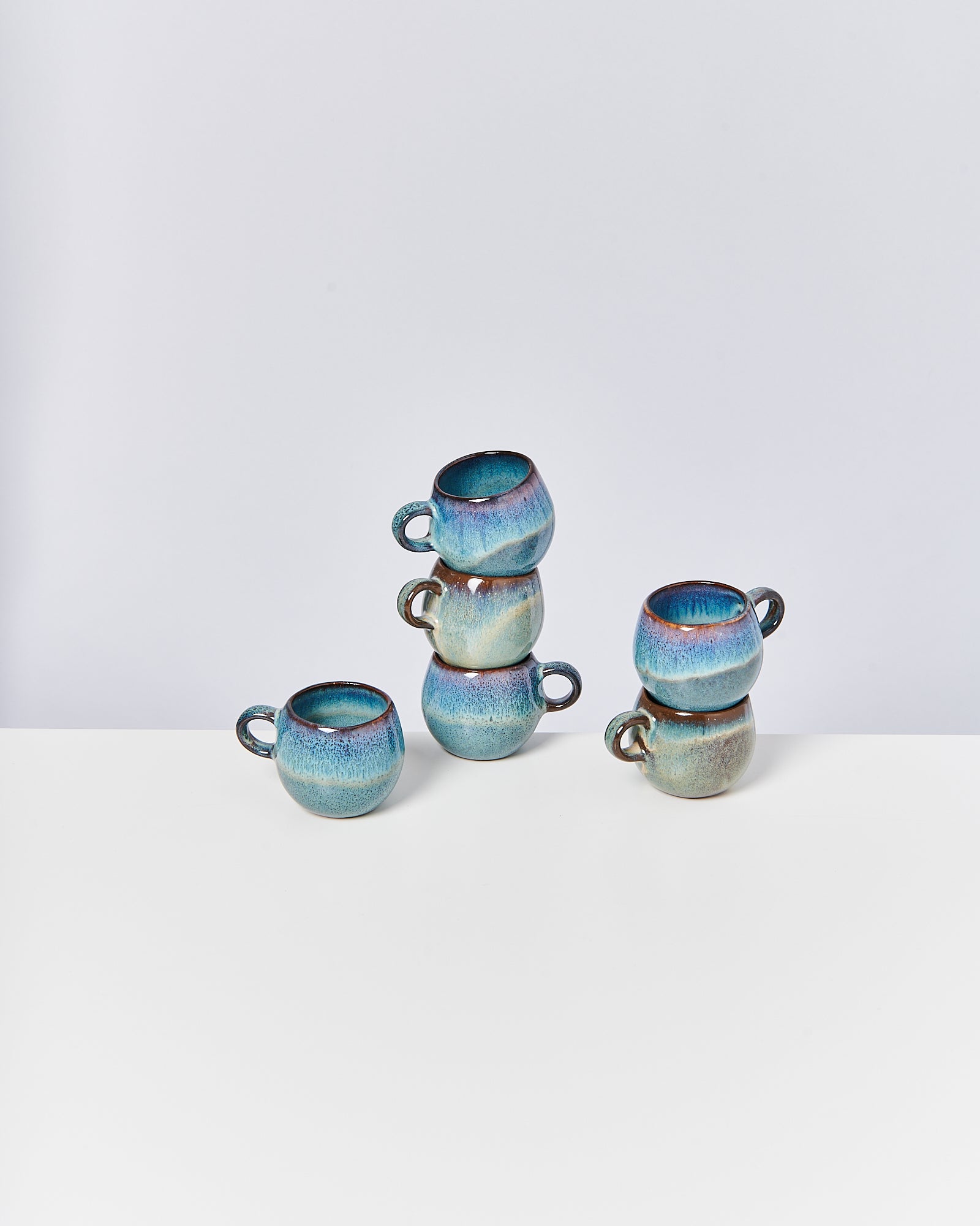 Vier blaue, gestapelte Tassen auf einem weißen Tisch vor einem neutralen Hintergrund.