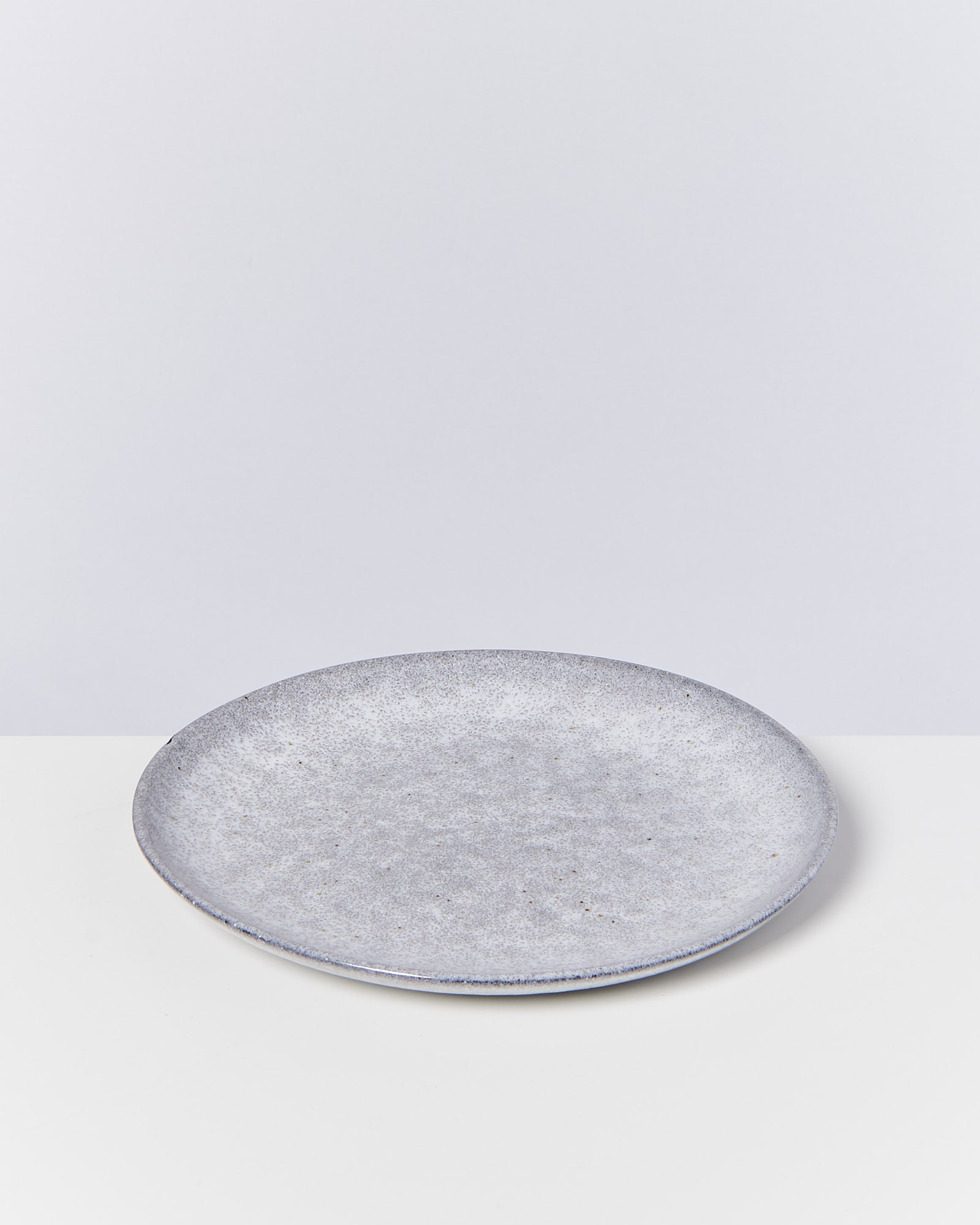 Grauer, runder Keramikteller auf weißem Hintergrund.