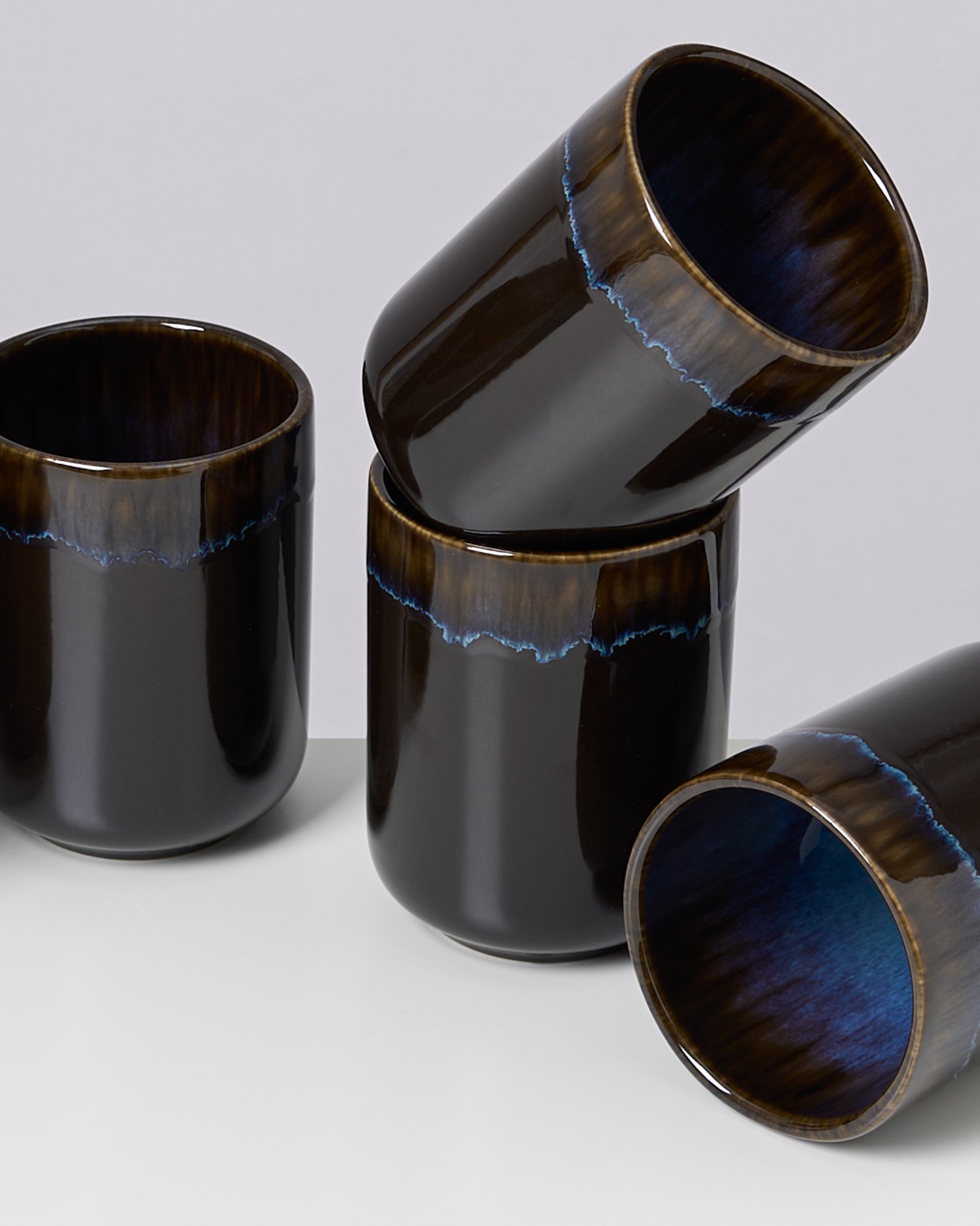 Vier schwarze, glänzende Keramikbecher mit blauer Innenseite und blauem Rand, teils übereinander gestapelt.