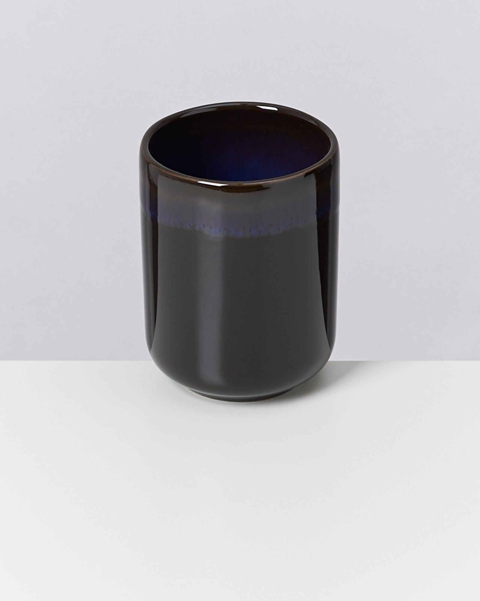 Schwarze, glänzende Keramiktasse mit einem dunkelblauen Rand auf einem weißen Hintergrund.