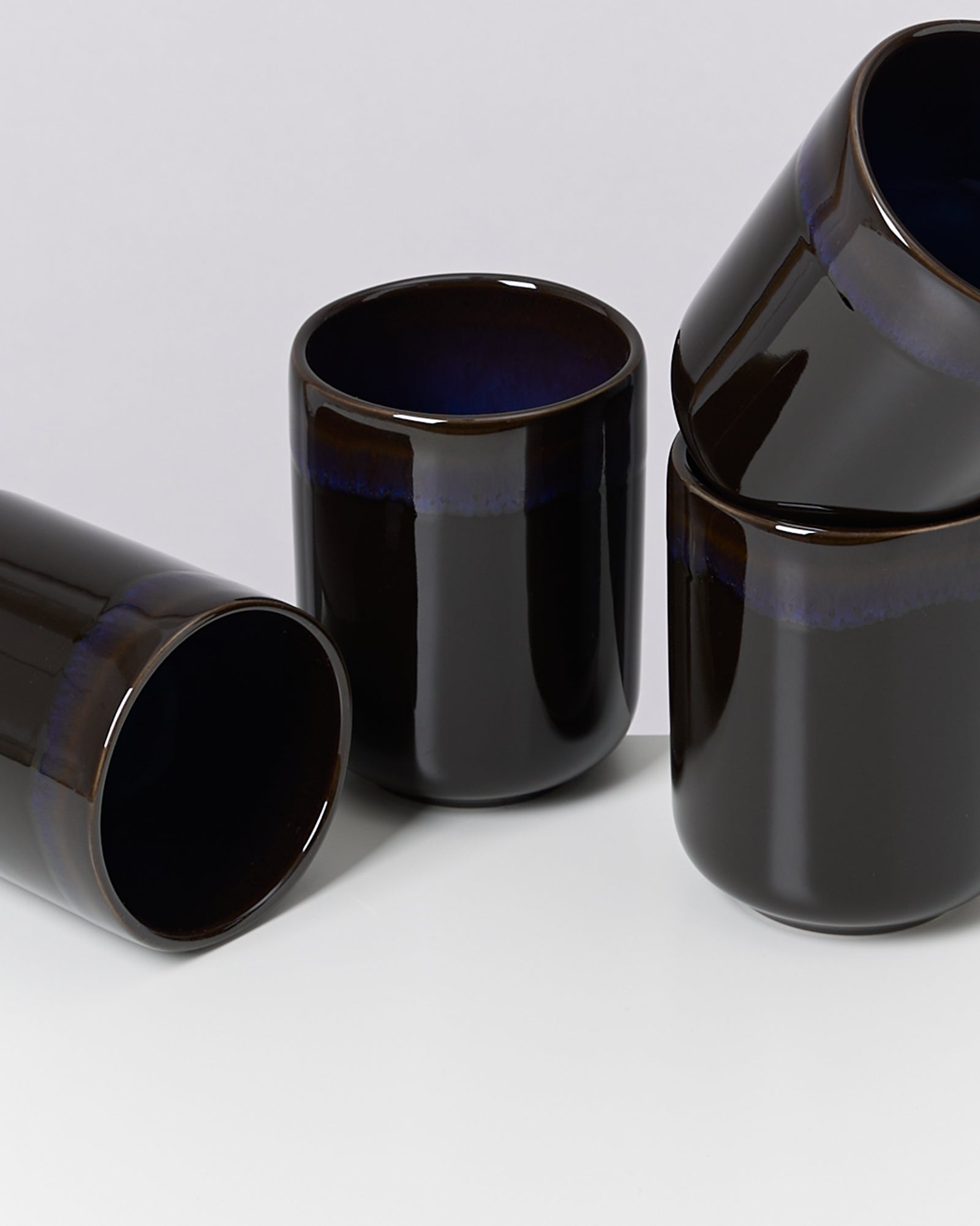 Vier schwarze Keramiktassen mit glänzender Oberfläche, zwei aufrecht stehend und zwei leicht geneigt liegend.