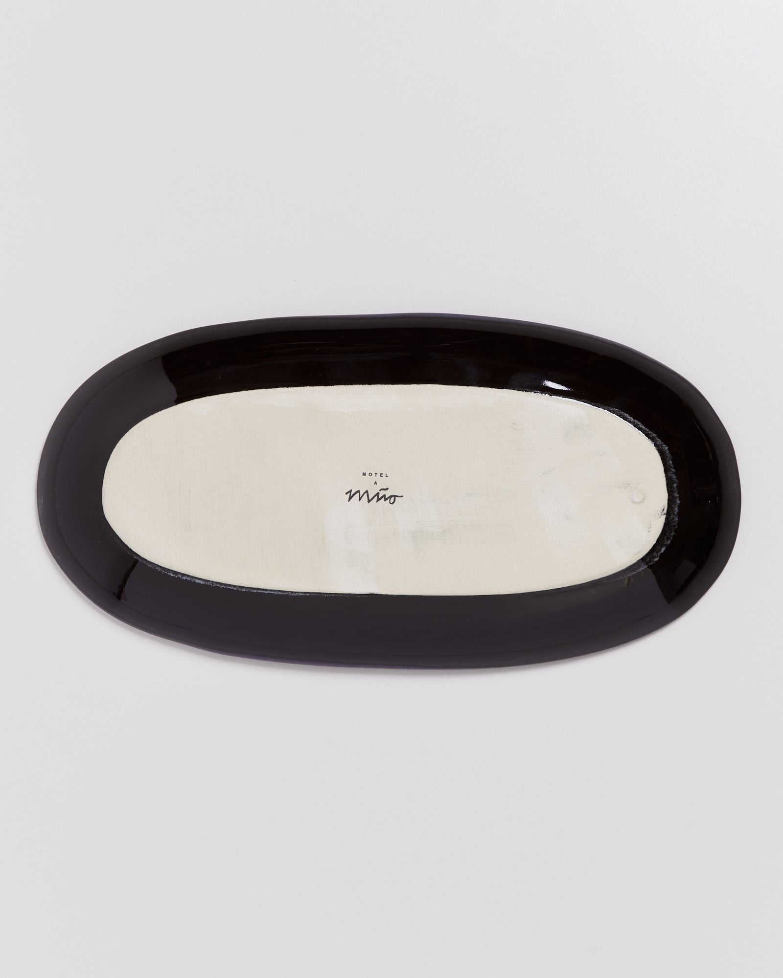 Weiße ovale Keramikplatte mit schwarzem Rand und der Aufschrift "HOTEL A Miro" auf der Unterseite.