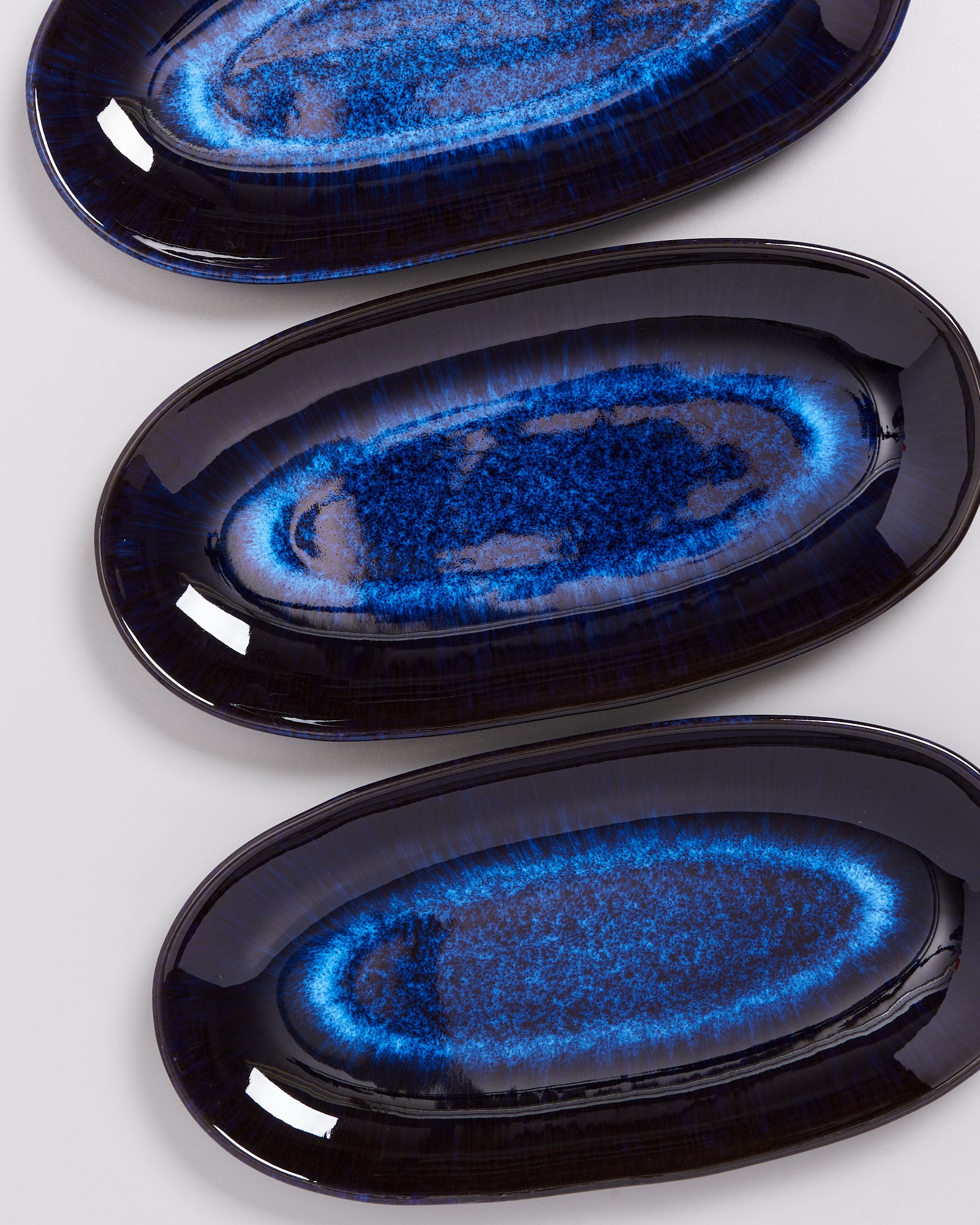 Drei ovale Teller mit blauer, marmorierter Glasur auf hellem Hintergrund.