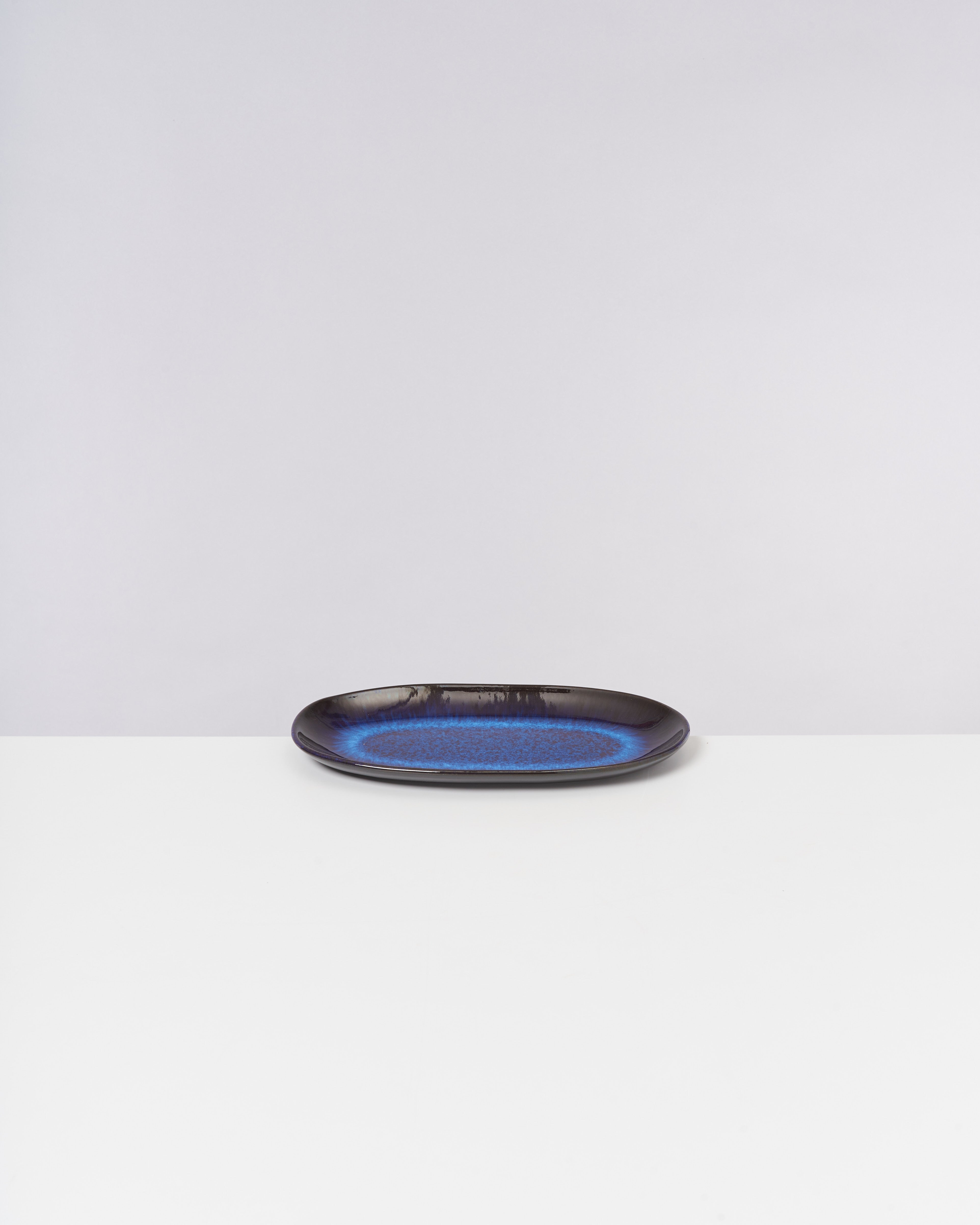 Schwarzer Teller mit blauem Muster auf weißem Untergrund vor grauem Hintergrund.