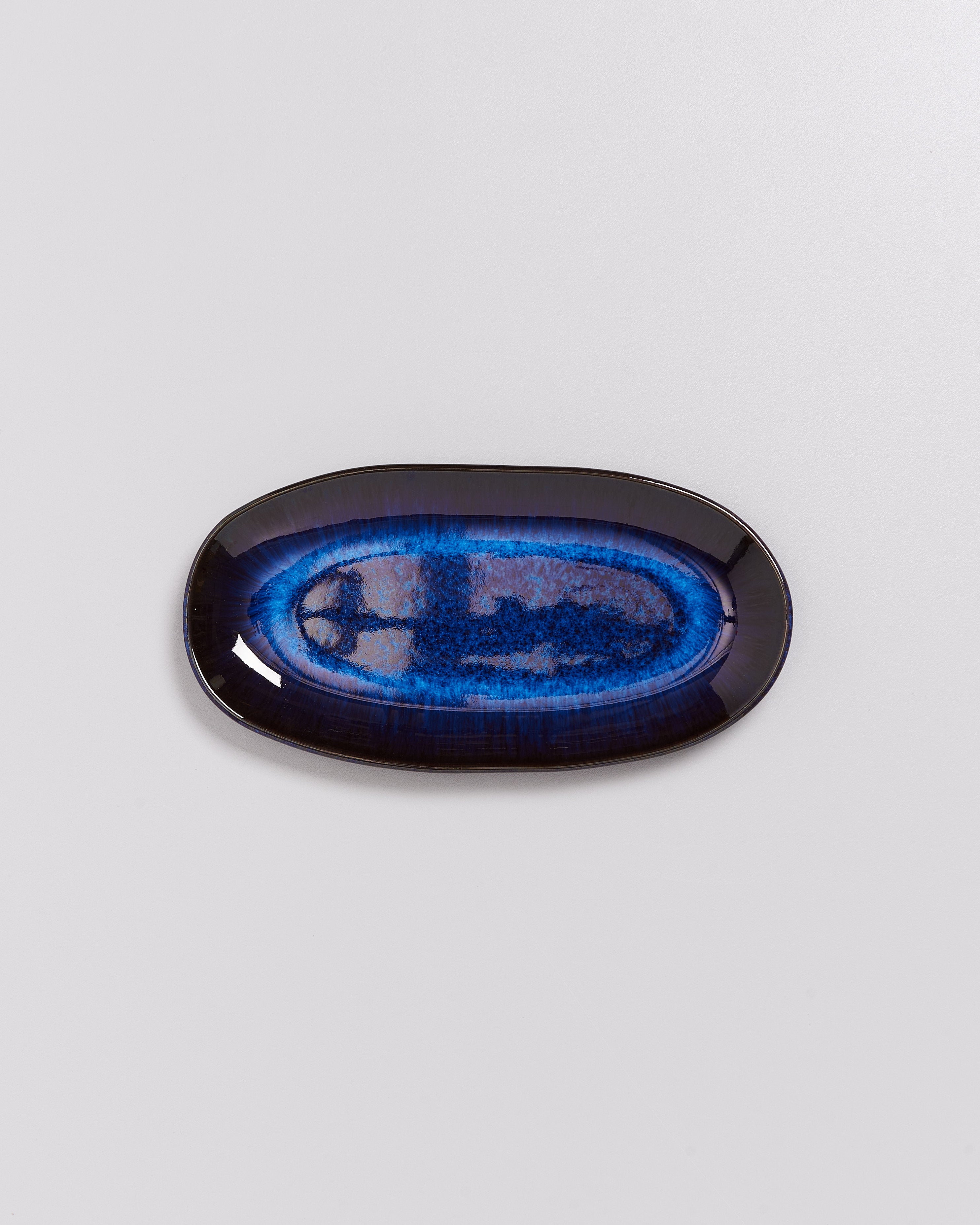 Ovale Keramikschale mit einem blauen und schwarzen Muster auf weißem Hintergrund.