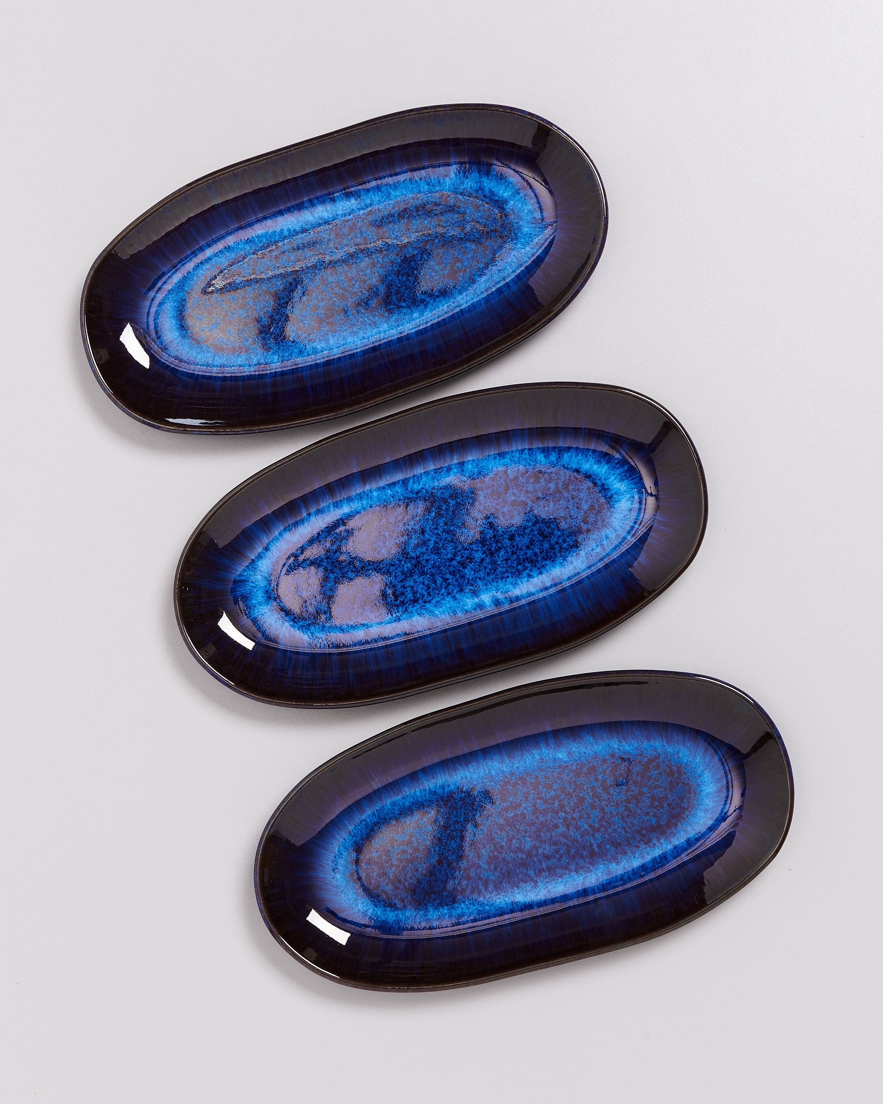Drei ovale Teller mit blauer, marmorierter Glasur auf hellem Hintergrund.