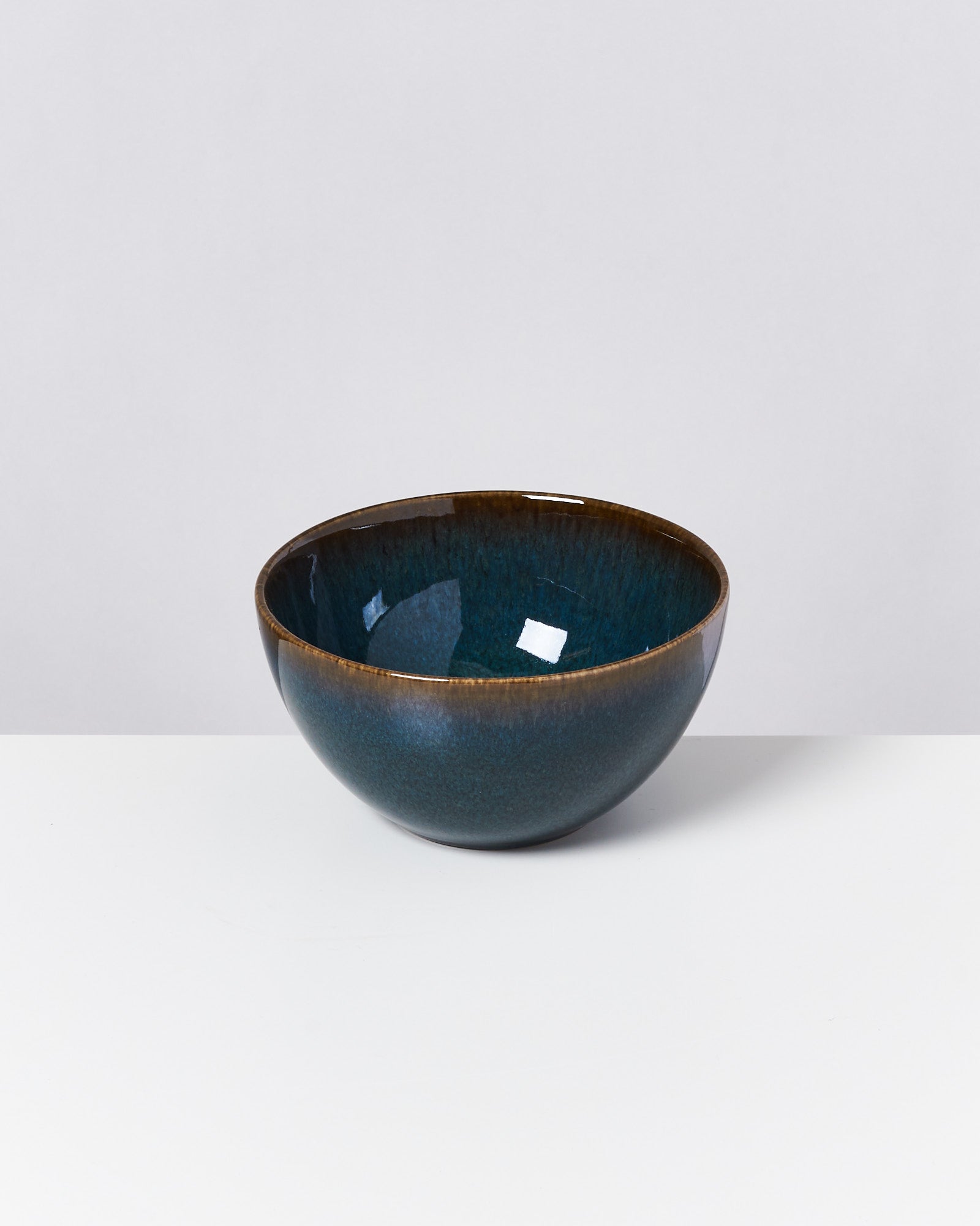 Blaue Keramikschüssel mit glänzender Oberfläche steht auf einem weißen Tisch vor neutralem Hintergrund.