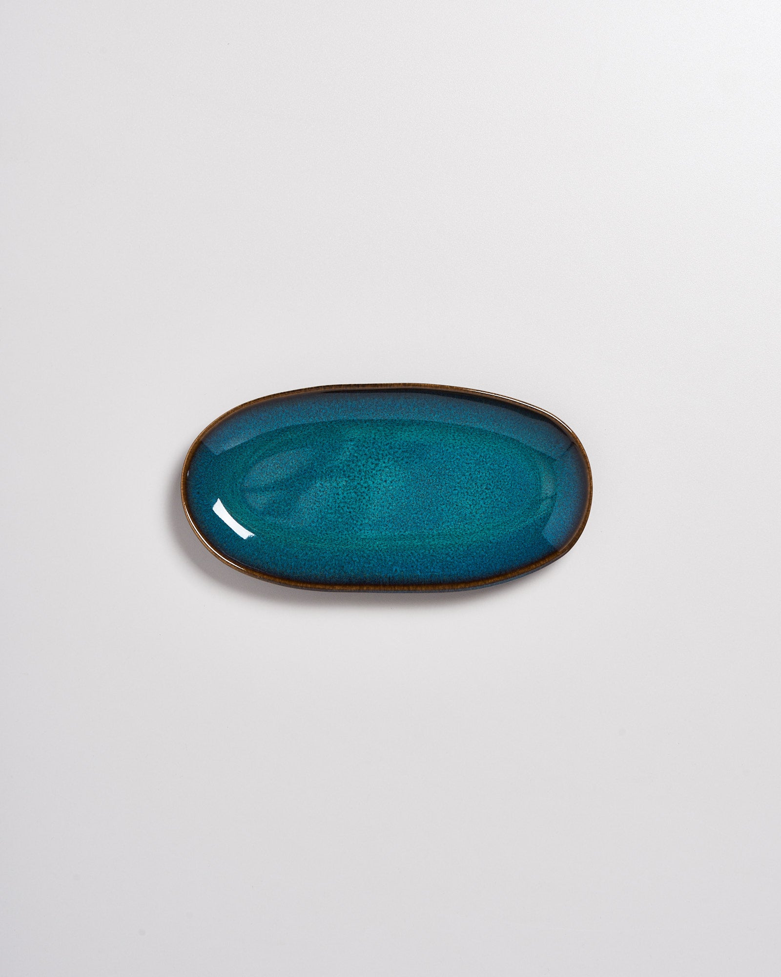 Ovaler, blaugrüner Keramikteller mit leicht glänzender Oberfläche auf grauem Hintergrund.