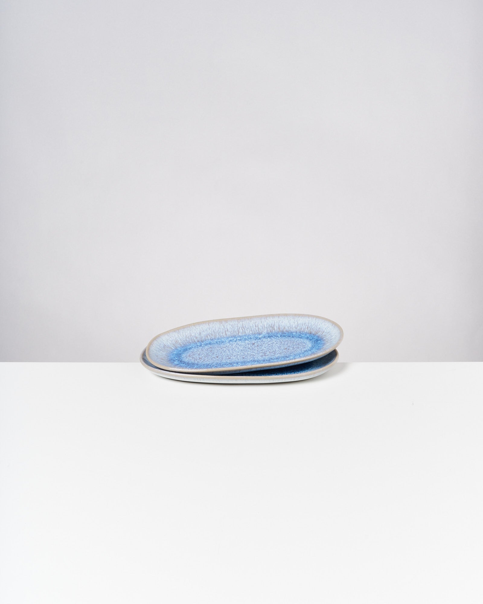 Zwei blau marmorierte Teller liegen übereinander auf einem weißen Tisch vor einem neutral grauen Hintergrund.