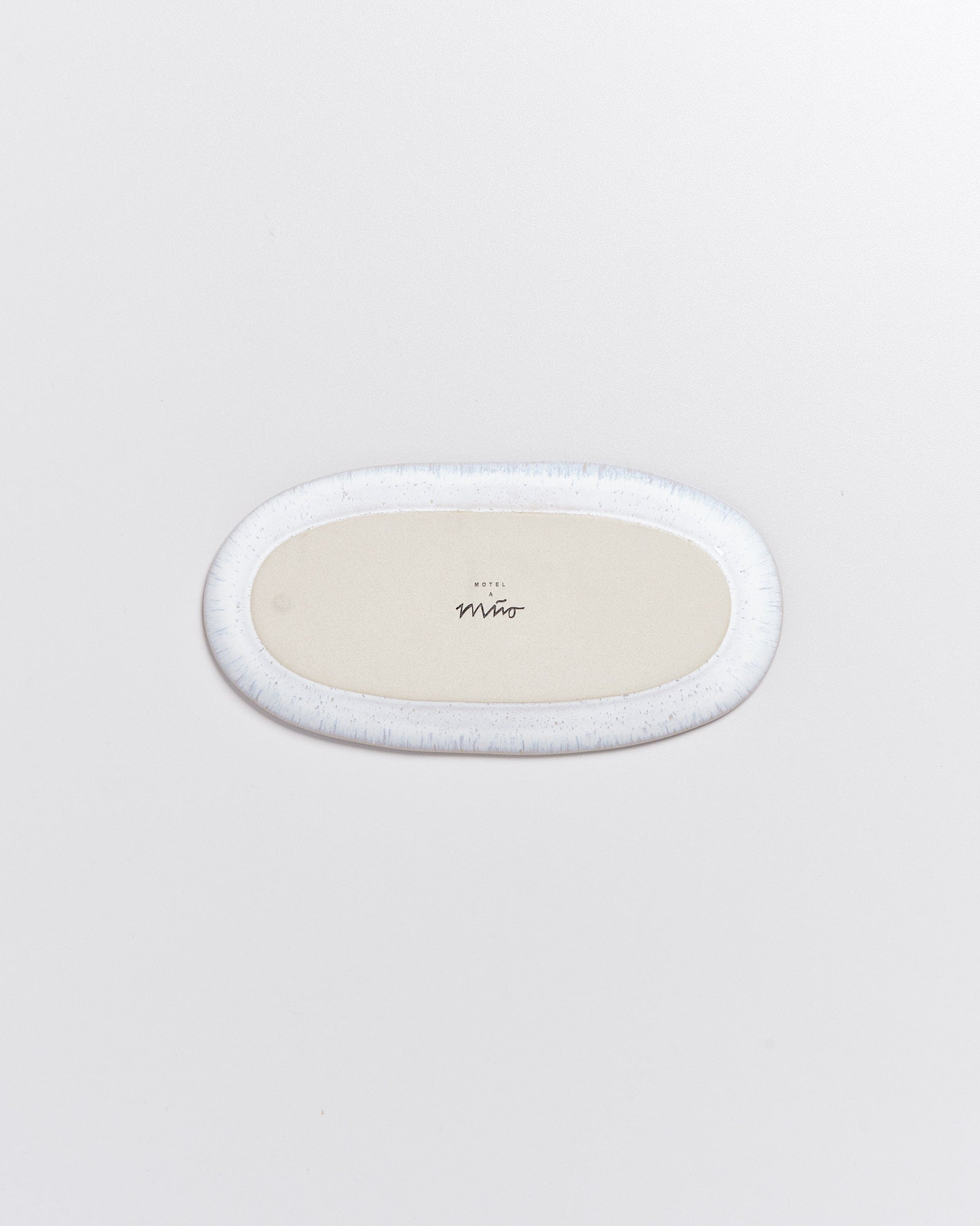 Ovale weiße Untertasse mit Hotel Miwo Beschriftung in der Mitte auf weißem Hintergrund.