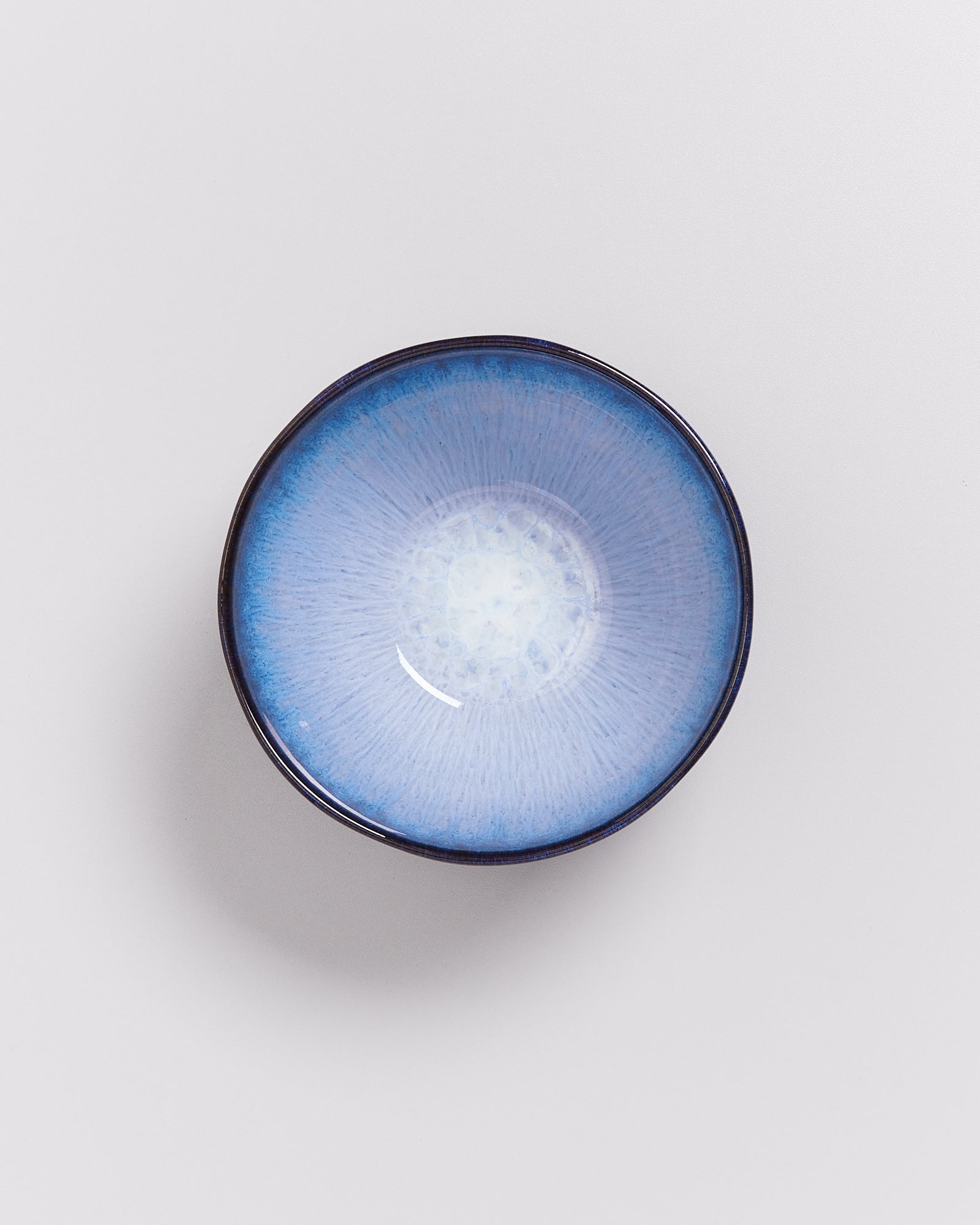 Blaue Keramikschale mit dunklem Rand auf hellem Hintergrund, zentral von oben fotografiert.