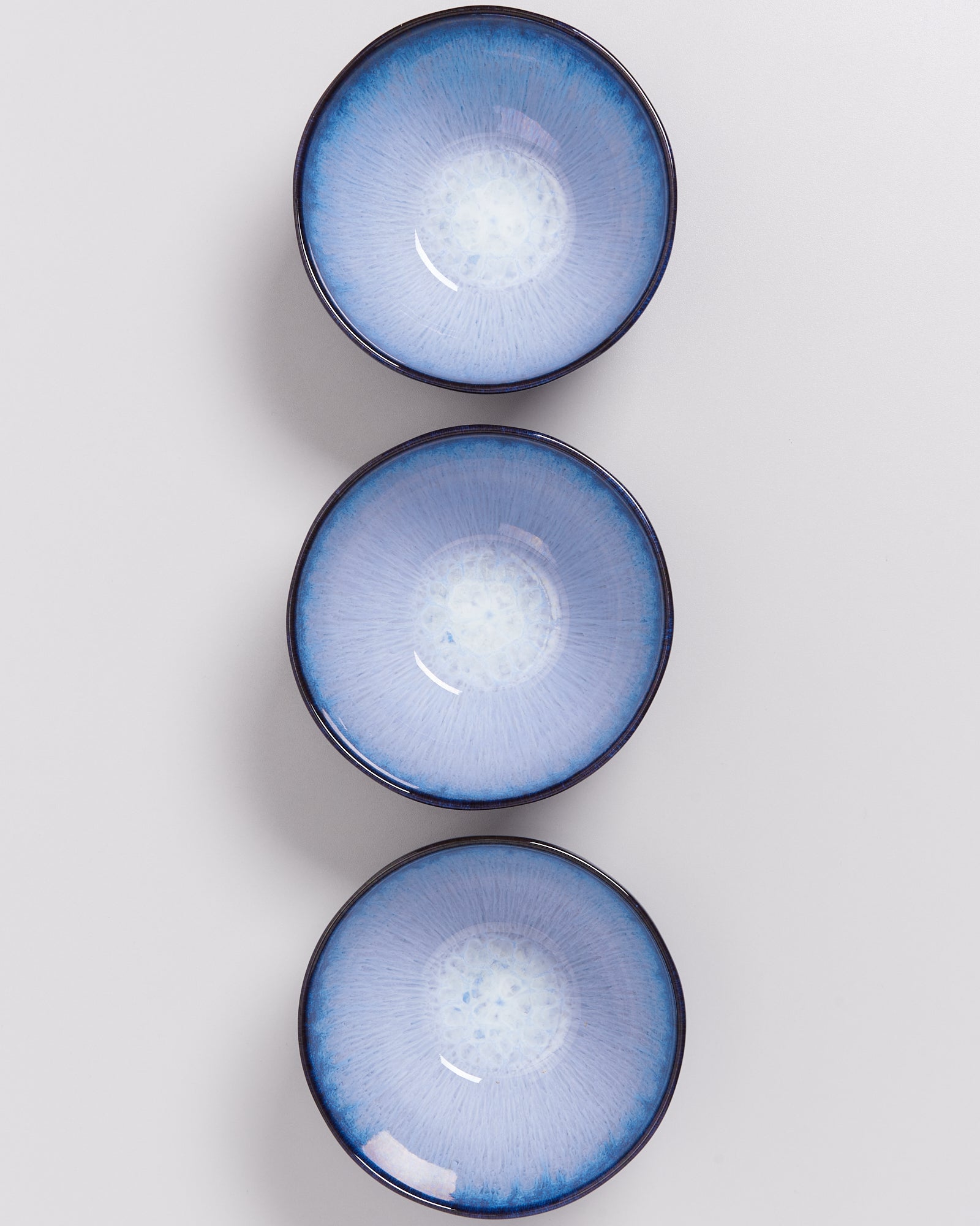 Drei blaue, runde Teller mit weißem Zentrum auf weißem Hintergrund angeordnet.