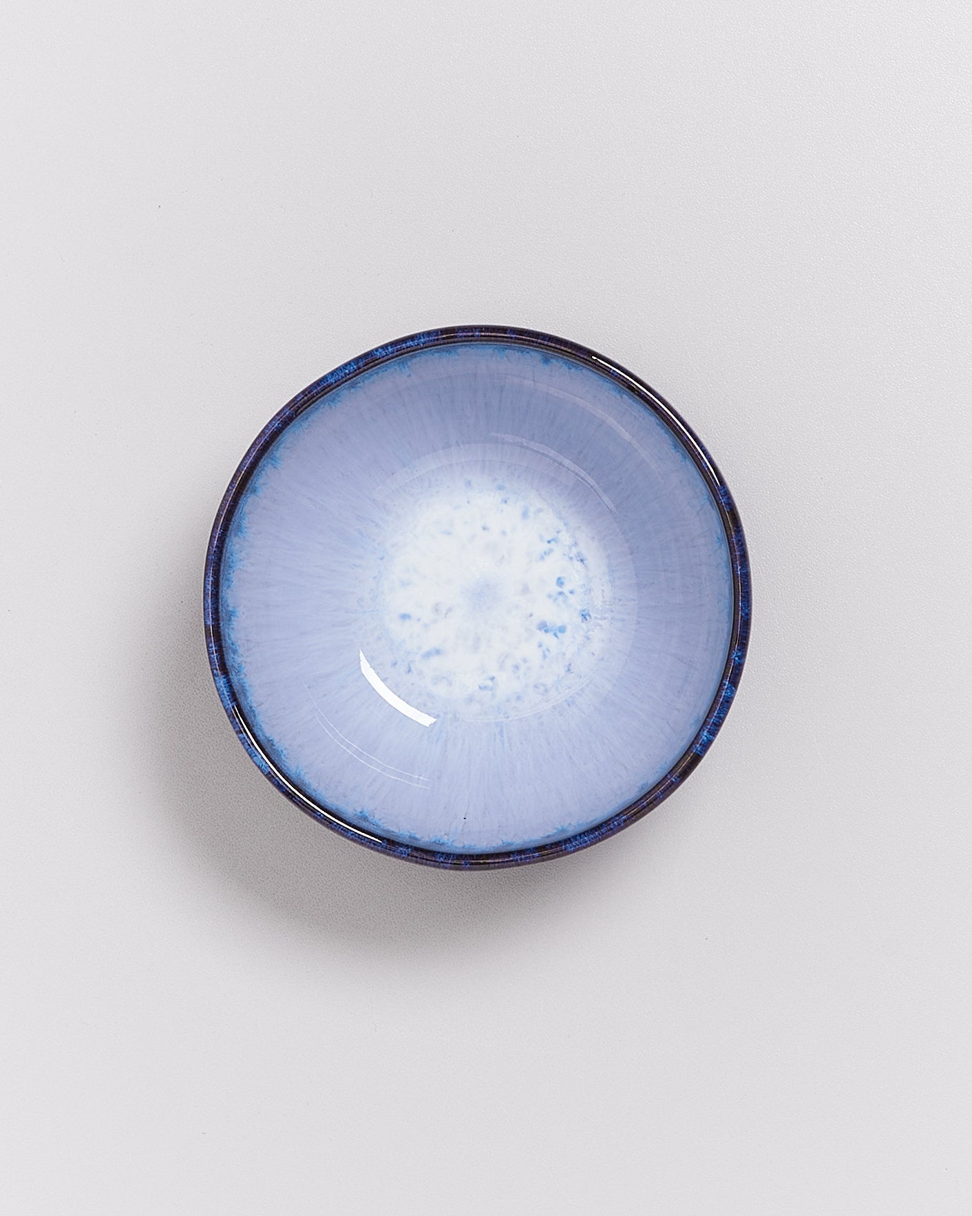 Kleine, runde Schale mit blauer Glasur und weißem, gesprenkeltem Zentrum auf hellem Hintergrund.