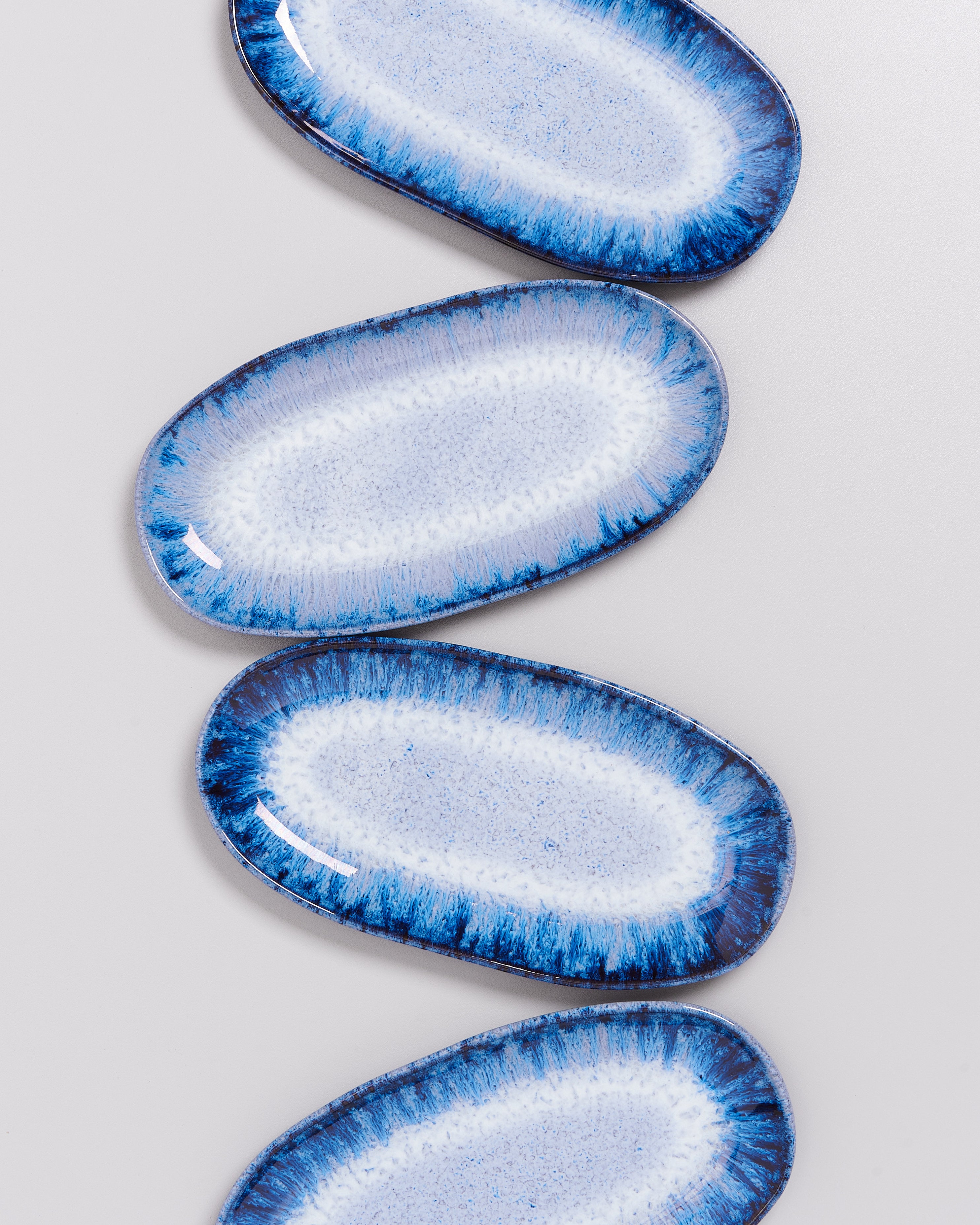 Vier ovale, blau-weiße Keramikteller mit Mustern liegen auf hellgrauem Hintergrund.