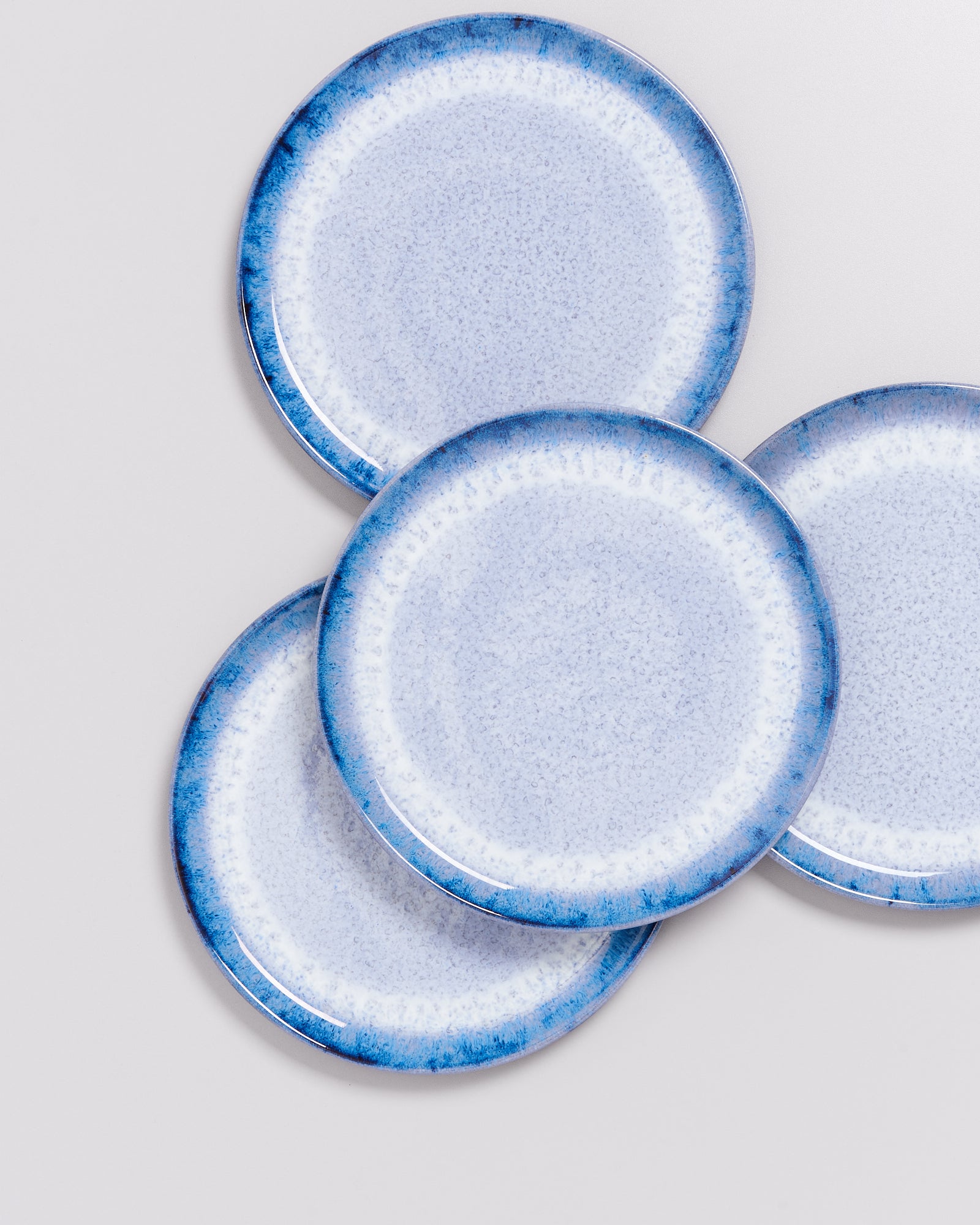 Vier blau-weiße Teller mit einem gesprenkelten Design sind leicht überlappend angeordnet.