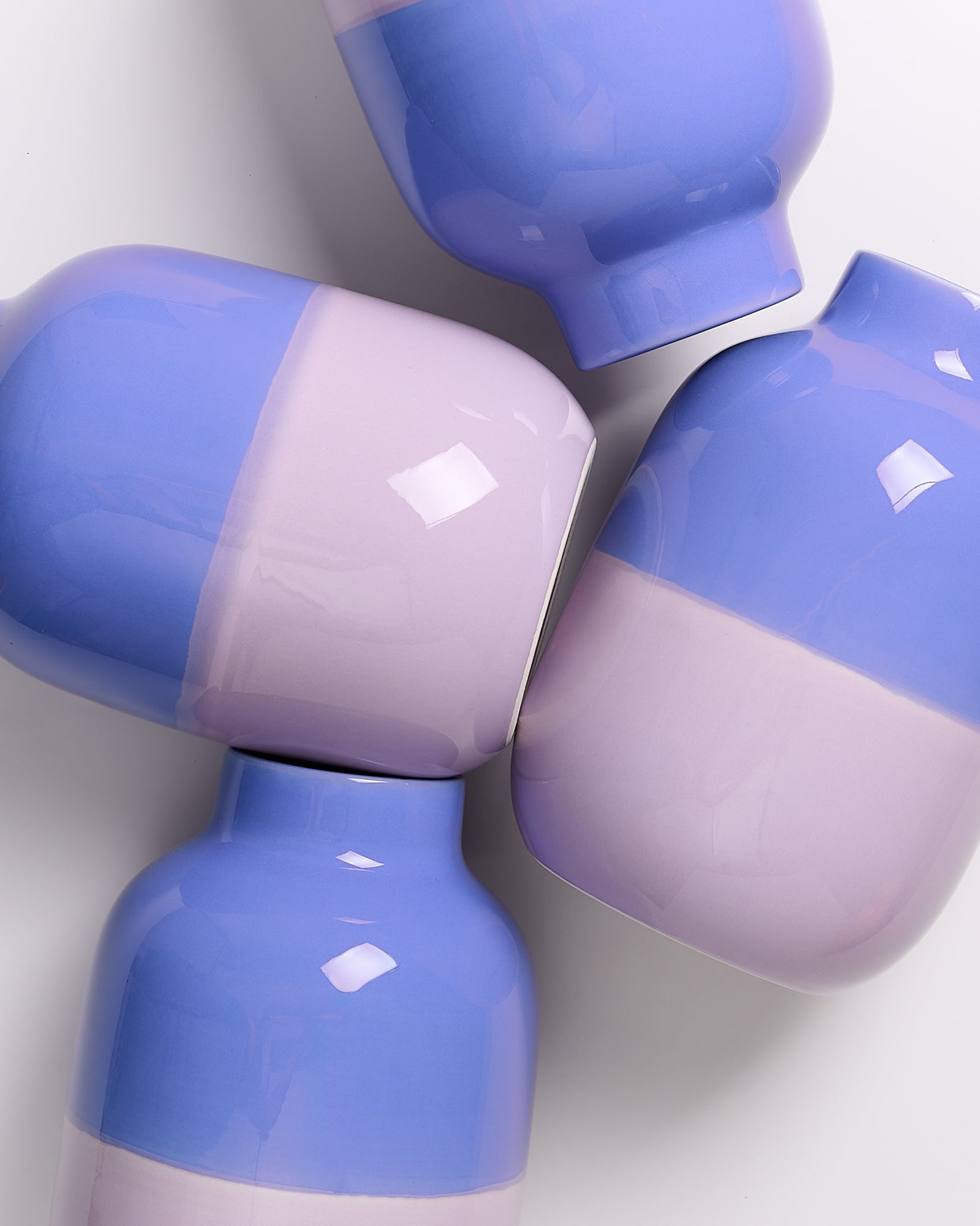 Vier lilafarbene Vasen mit glatter Oberfläche liegen auf einem weißen Hintergrund.