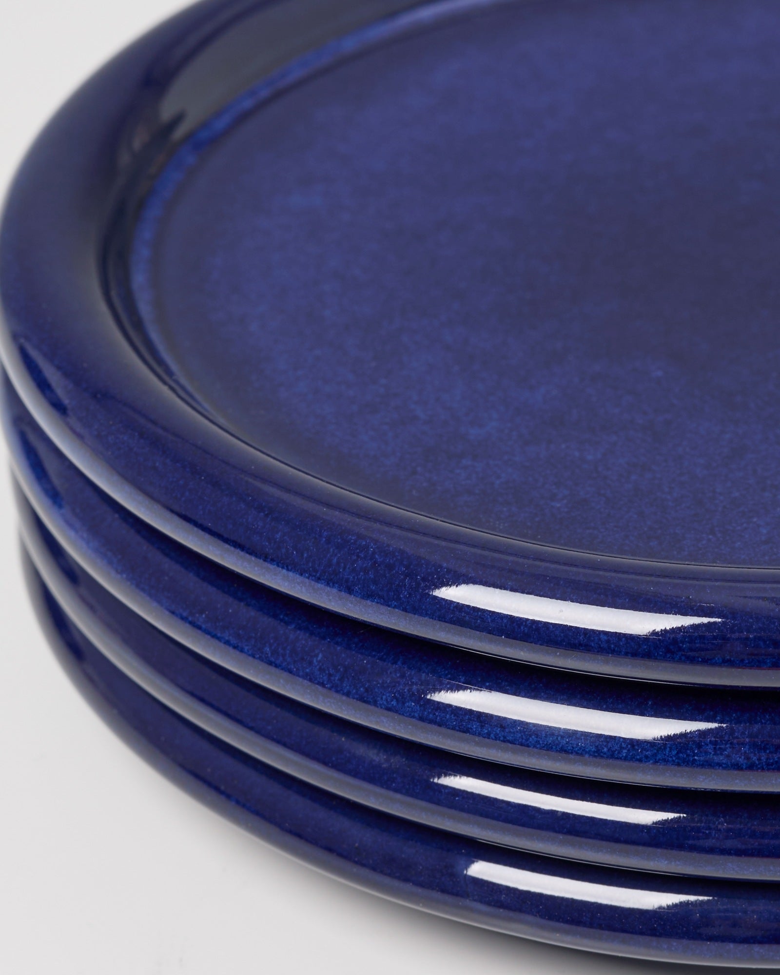 Ein Stapel von vier glänzenden, dunkelblauen Tellern auf einem weißen Hintergrund.