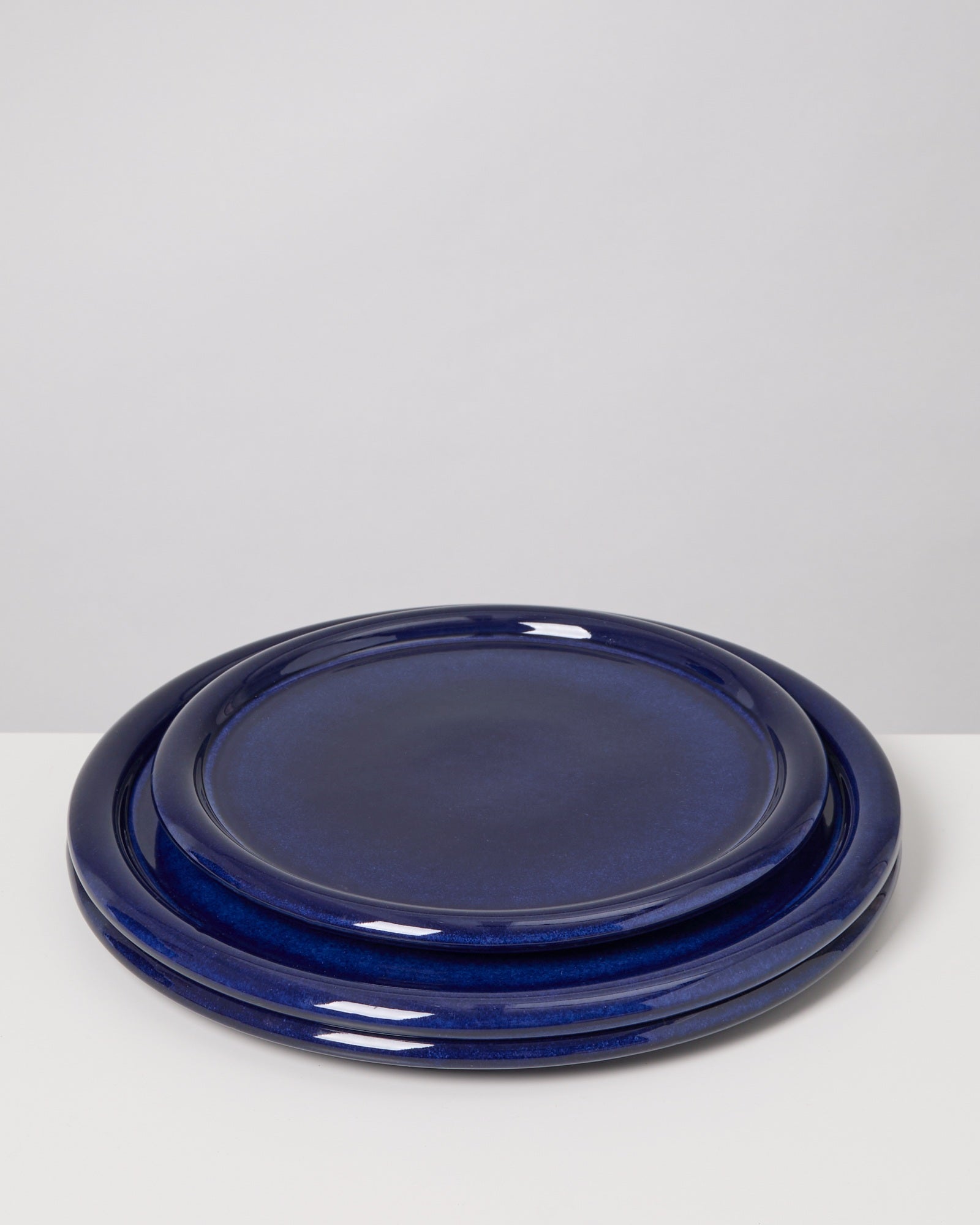 Drei dunkelblaue Keramikteller sind gestapelt und liegen auf einer weißen Oberfläche.