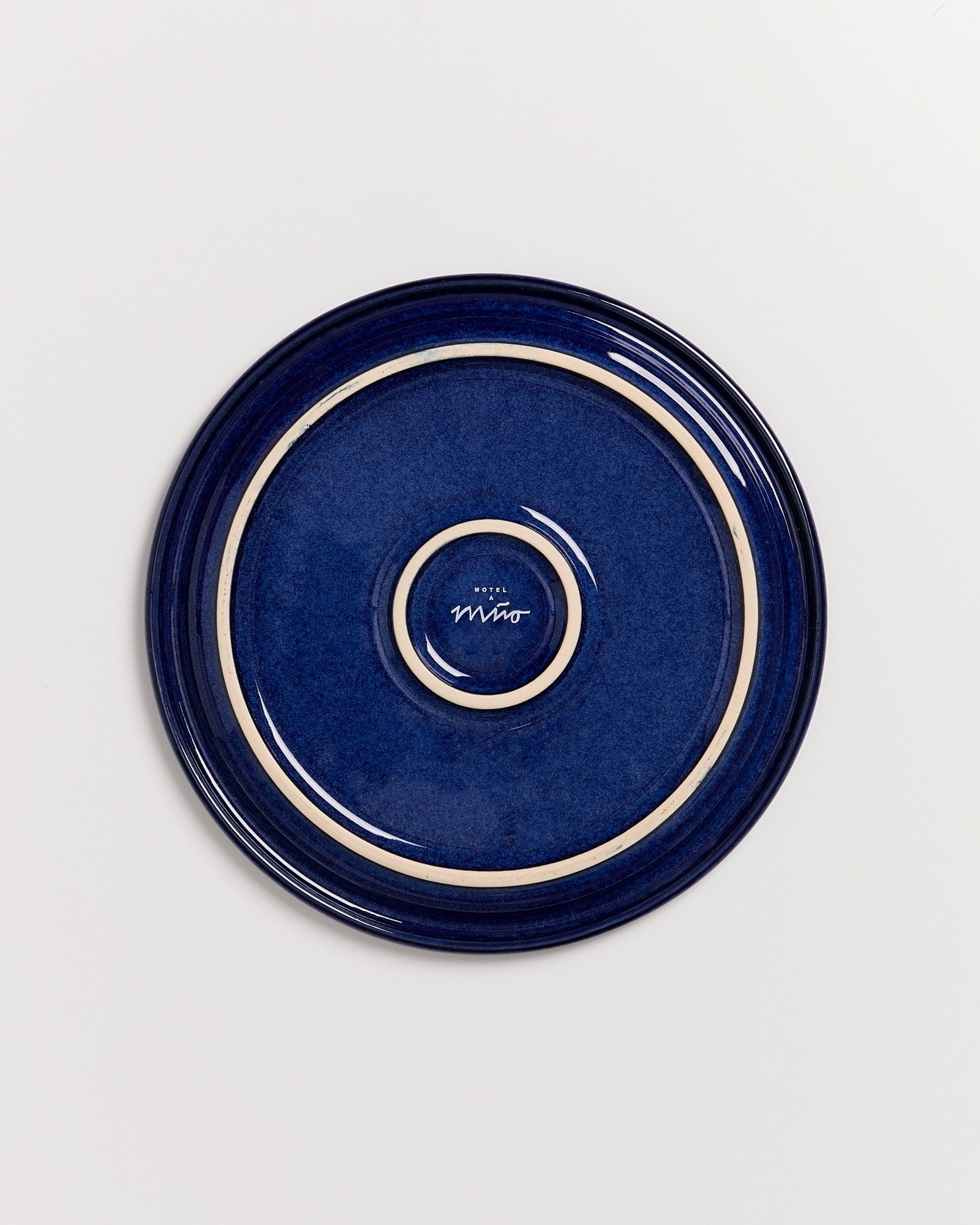 Blauer Keramikteller mit beigem Rand und der Aufschrift "Hotel Miró" in der Mitte, auf weißem Hintergrund.