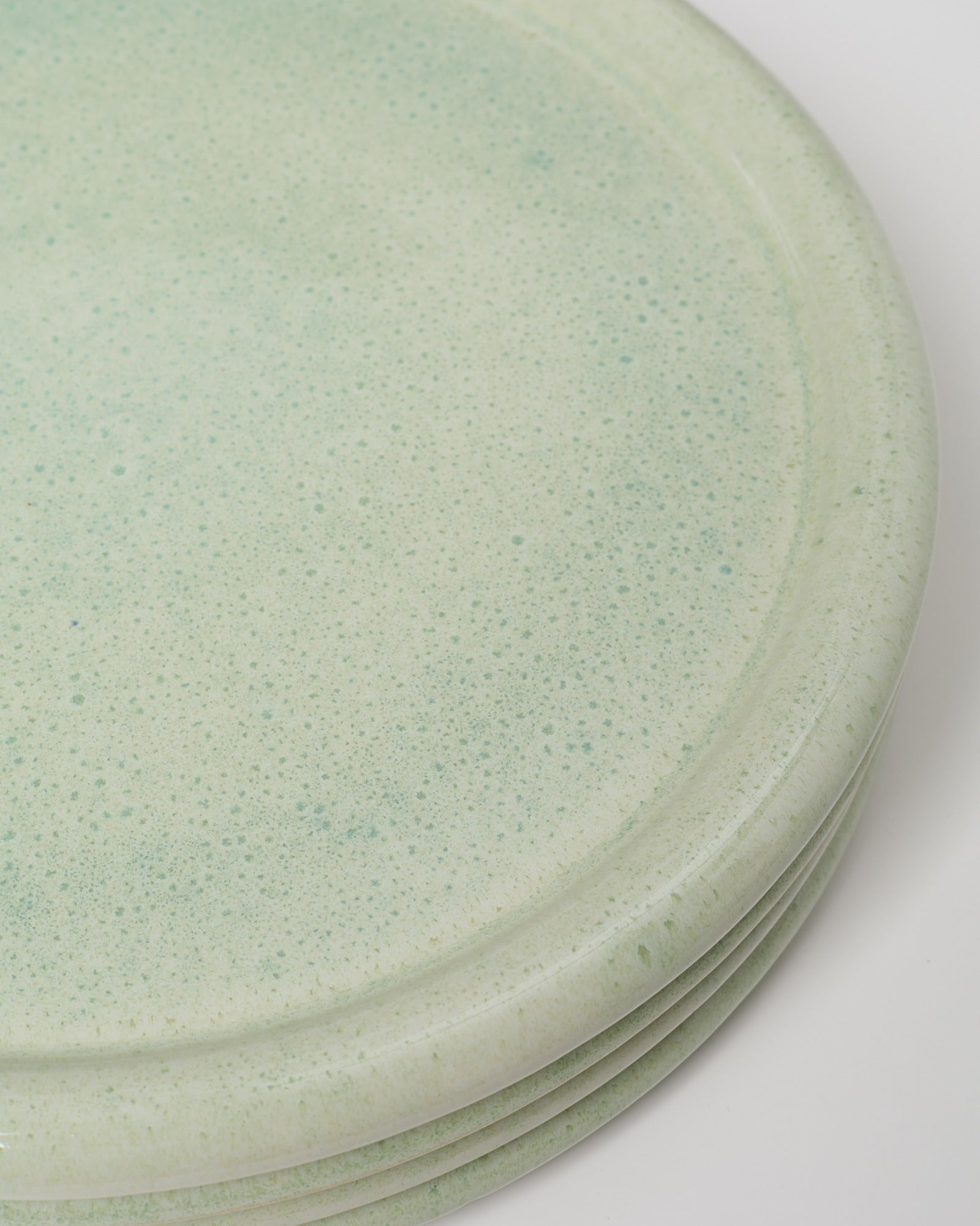 Detailaufnahme grün gesprenkelter, gestapelter Keramikteller auf weißem Hintergrund.