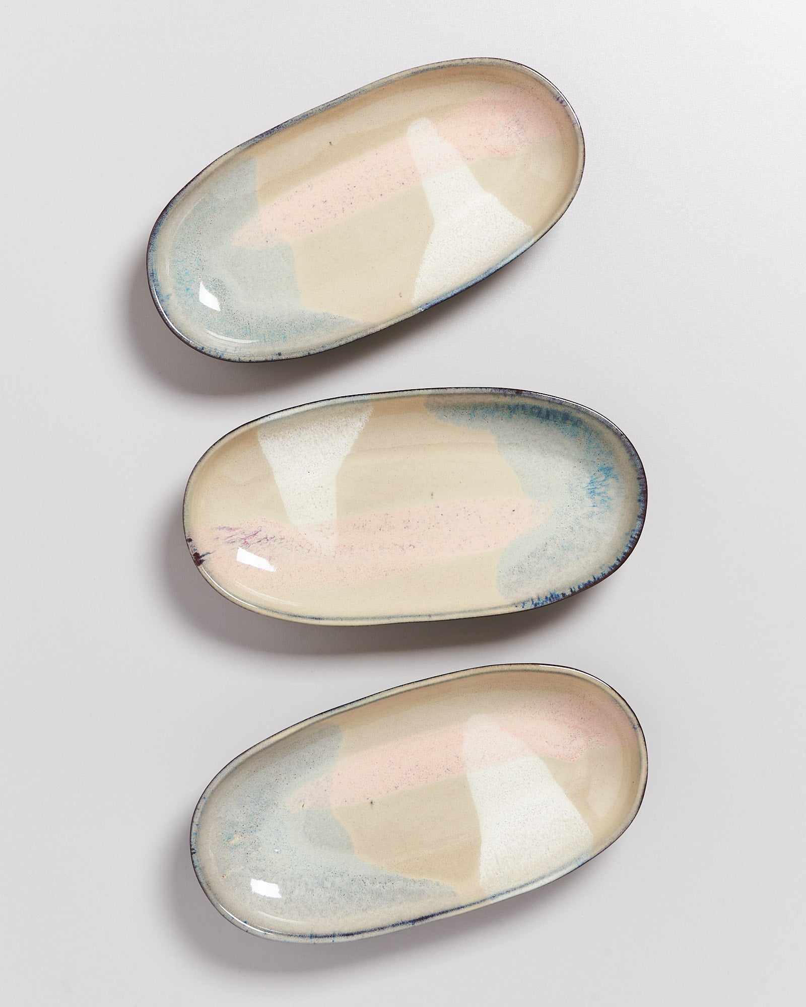 Drei ovale, gemusterte Keramikteller mit weichen Pastelltönen auf einer weißen Oberfläche platziert.