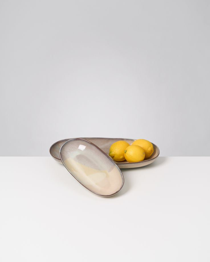 Zwei ovale Schalen auf einem weißen Tisch, eine ist leer und die andere enthält mehrere Zitronen.