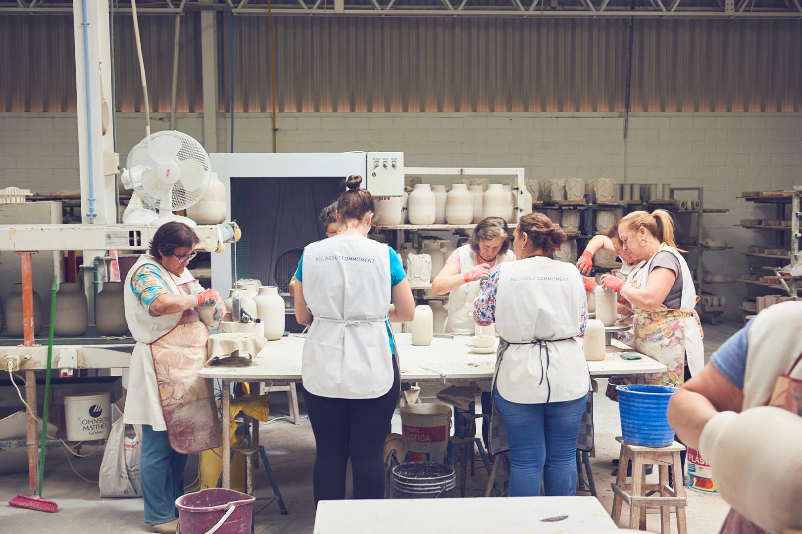 Menschen arbeiten in einer Keramikwerkstatt, formen und bearbeiten Tonvasen an einem Tisch.