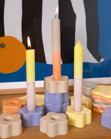 Bunte Kerzen in sternförmigen Haltern auf einem Tisch vor dekorativem Hintergrund.