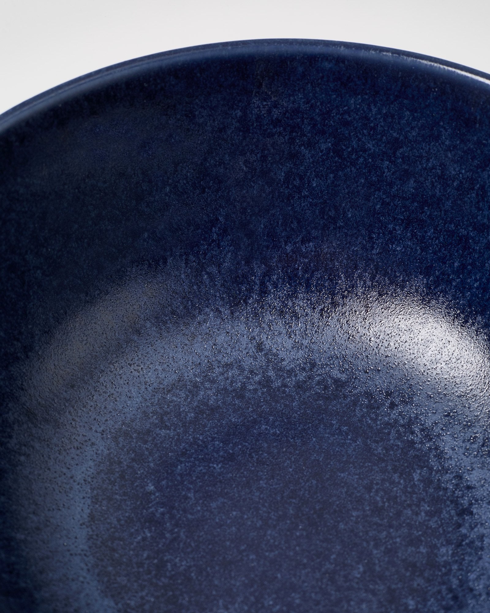 Nahaufnahme einer dunkelblauen, texturierten Rundung eines Tellers mit glänzender Oberfläche.