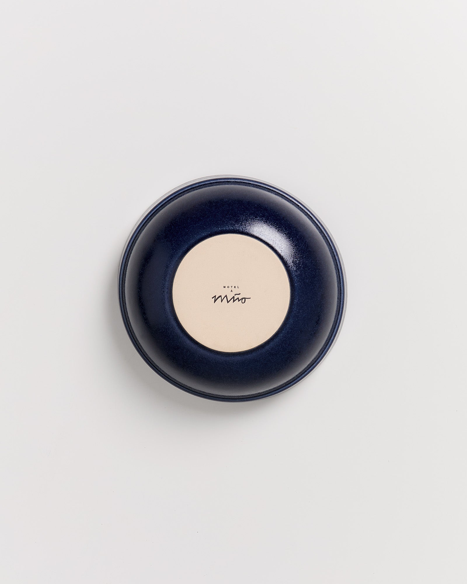 Rückseite eines tiefblauen Tellers mit einem beigen Kreis in der Mitte, der den Schriftzug "Hotel Miro" trägt.