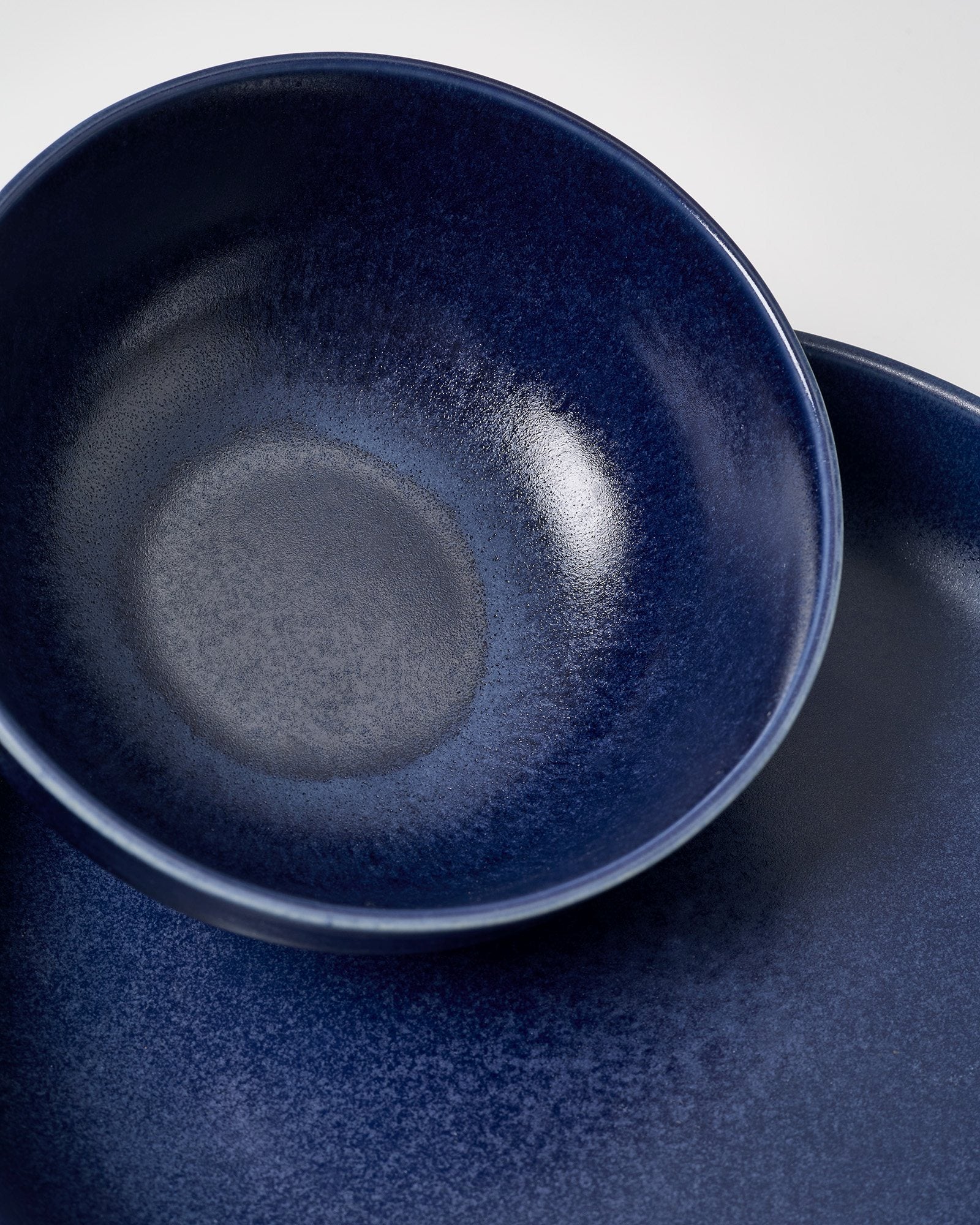 Dunkelblaue, glatte Keramikschale und Teller mit gesprenkeltem Muster.