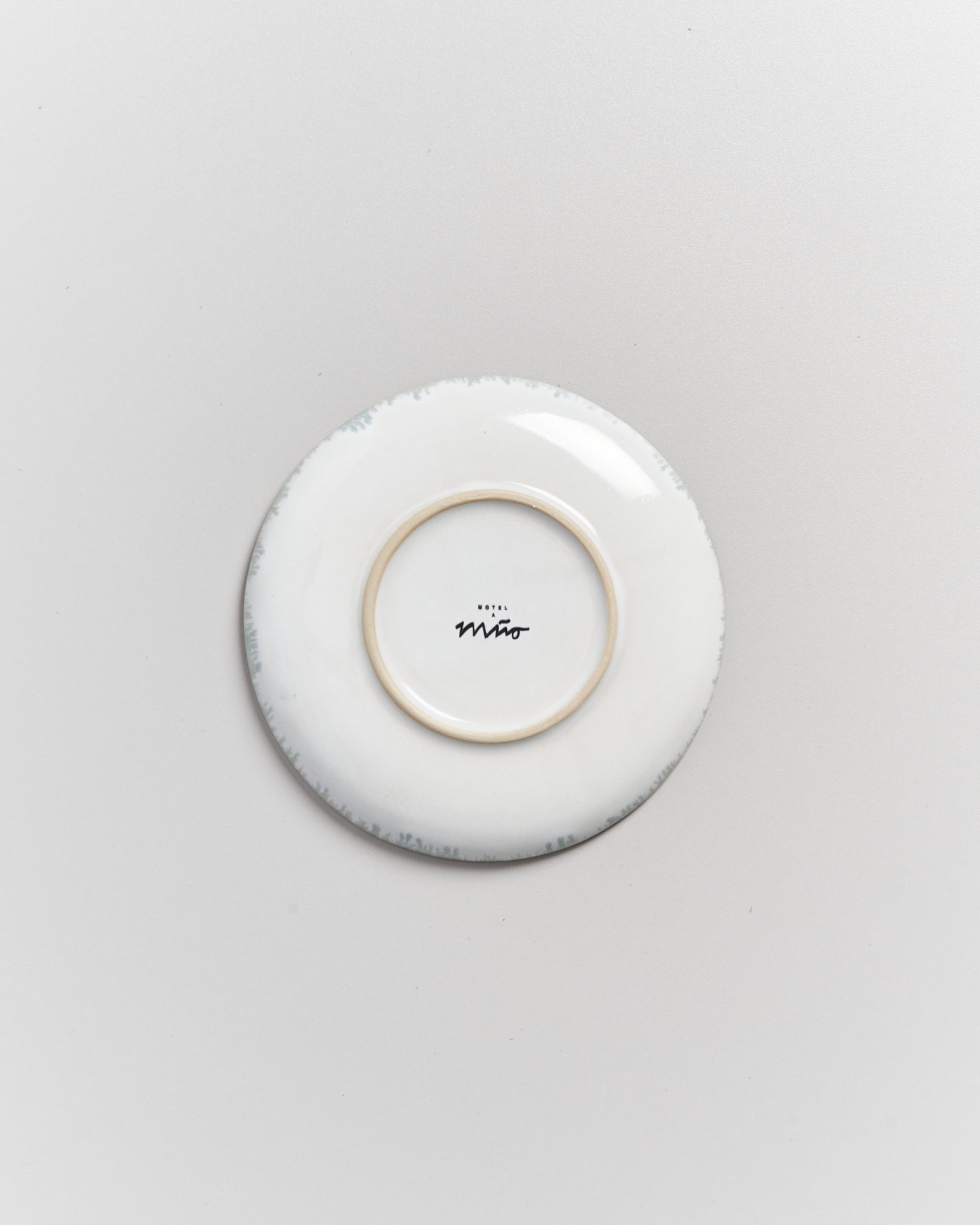 Weiße Unterseite eines Tellers mit einem Schriftzug in der Mitte auf einem hellgrauen Hintergrund.