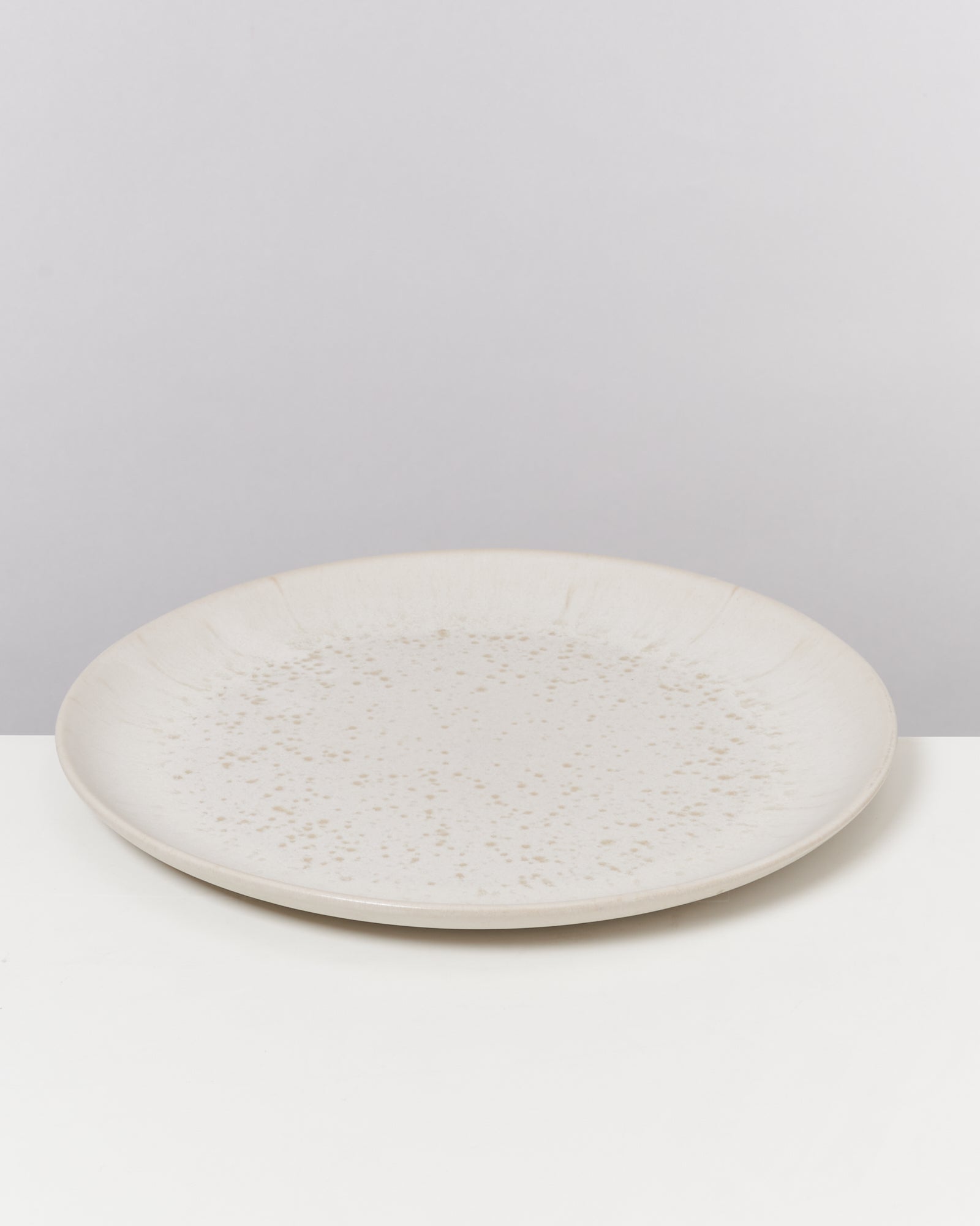 Beiger, keramischer Teller mit feinen Sprenkeln auf einem weißen Hintergrund.