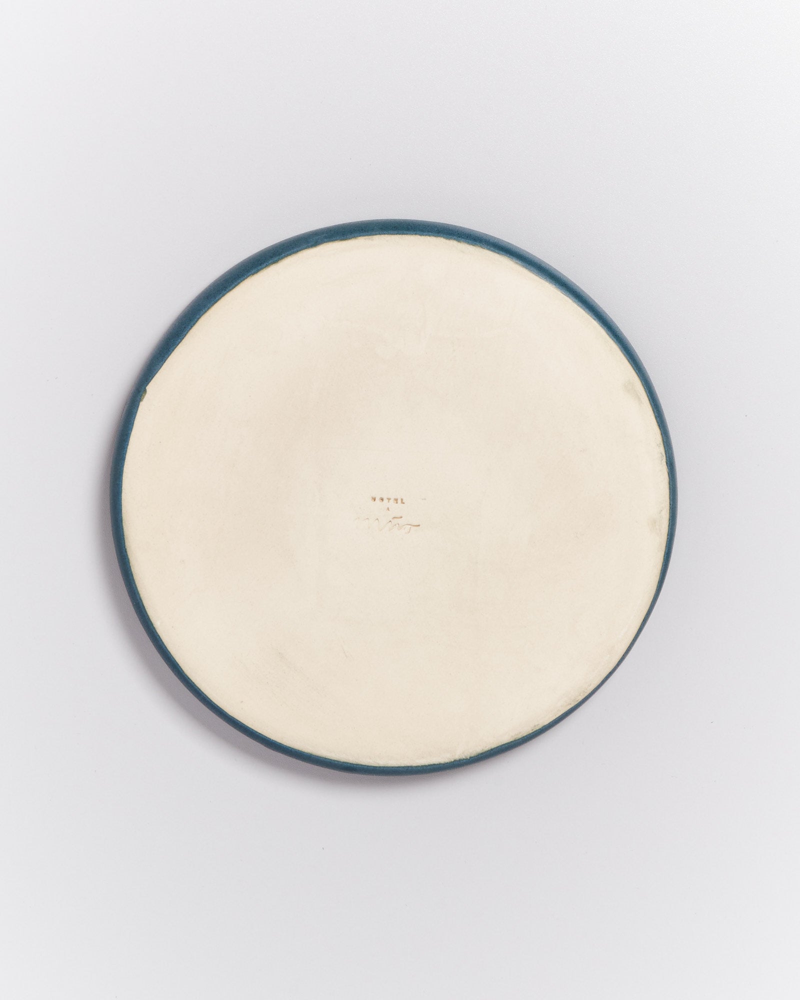 Rückseite eines runden Keramik-Tellers mit blauer Kante, auf hellem Hintergrund fotografiert.