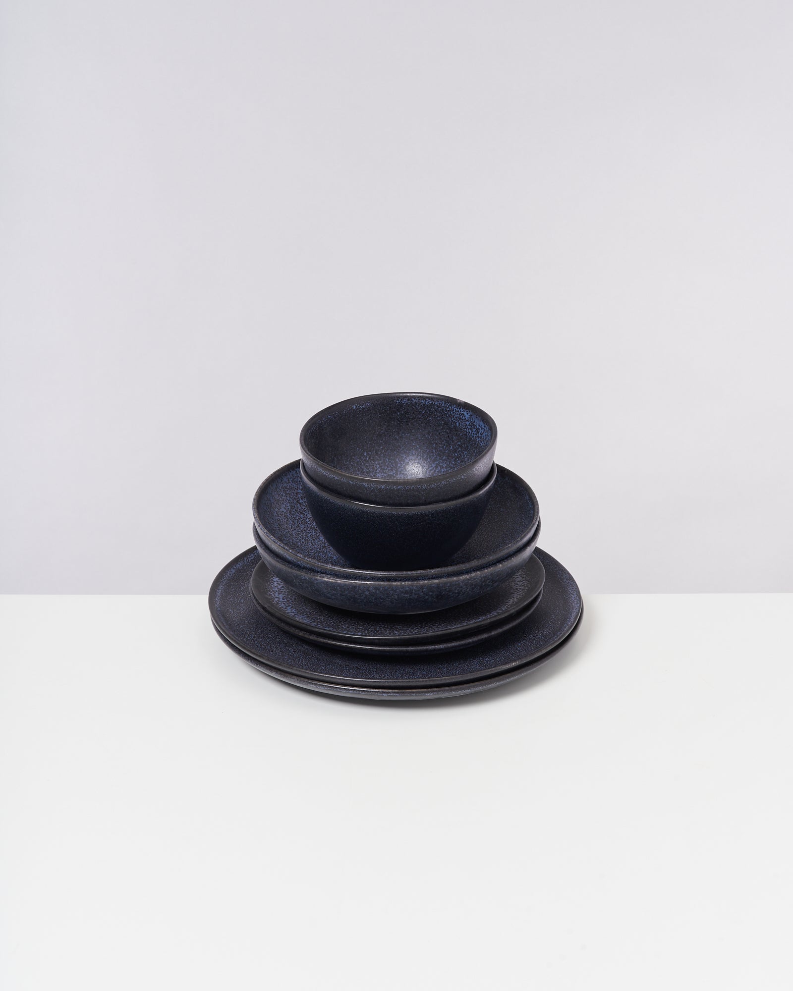 Ein Stapel schwarzer Keramikteller und Schüsseln steht auf einem weißen Tisch vor einem grauen Hintergrund.