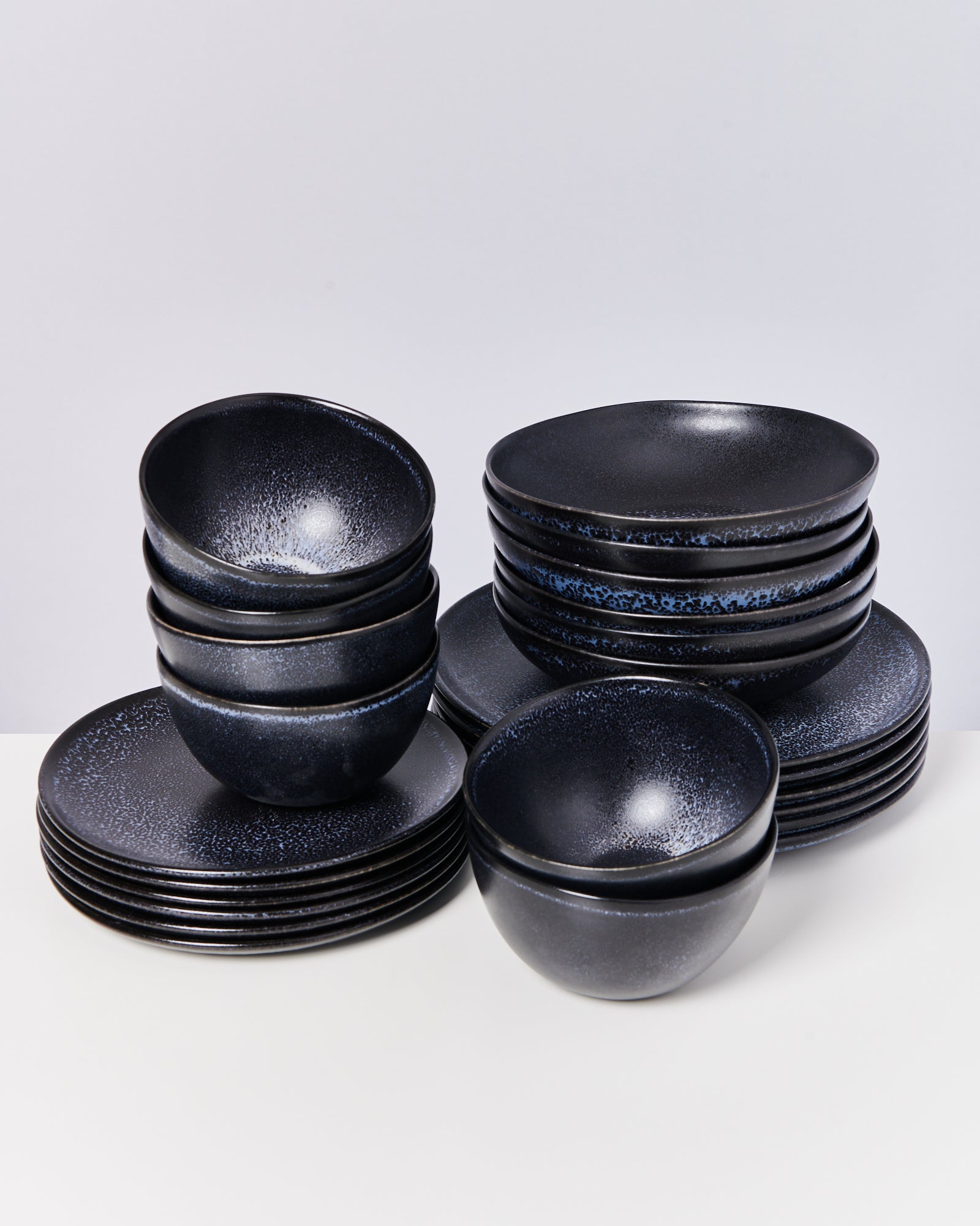 Ein Set aus dunklen, glänzenden Tellern und Schalen auf einem weißen Hintergrund.