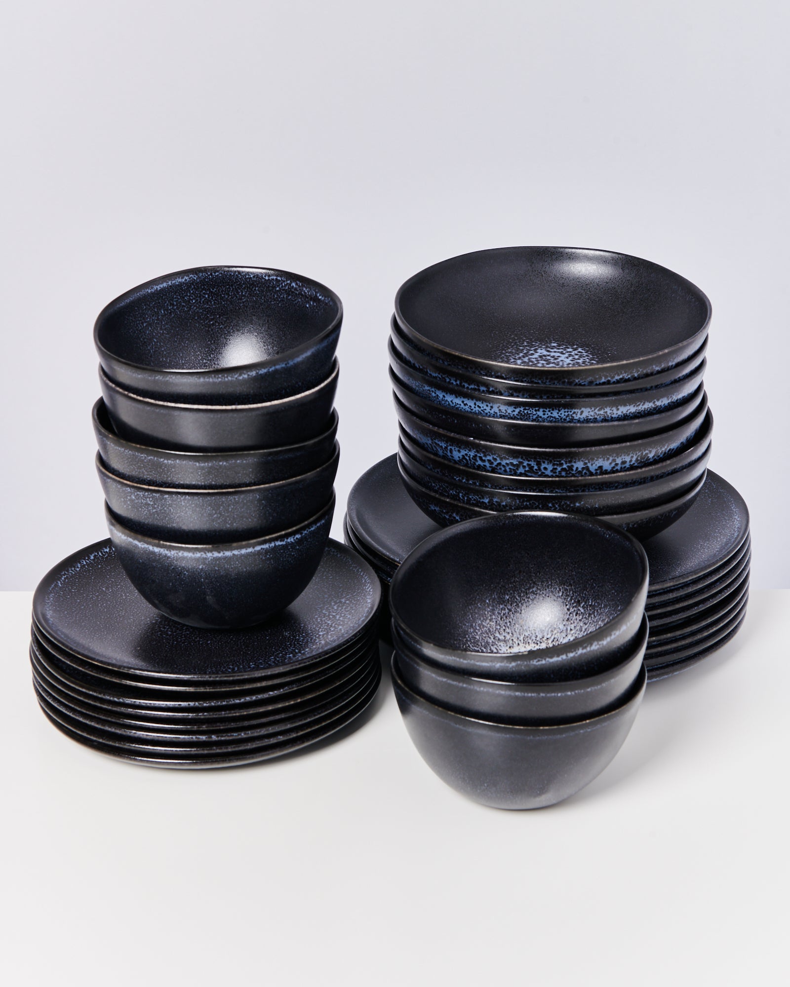 Schwarze Geschirrsets mit Schalen und Tellern auf weißem Hintergrund gestapelt.