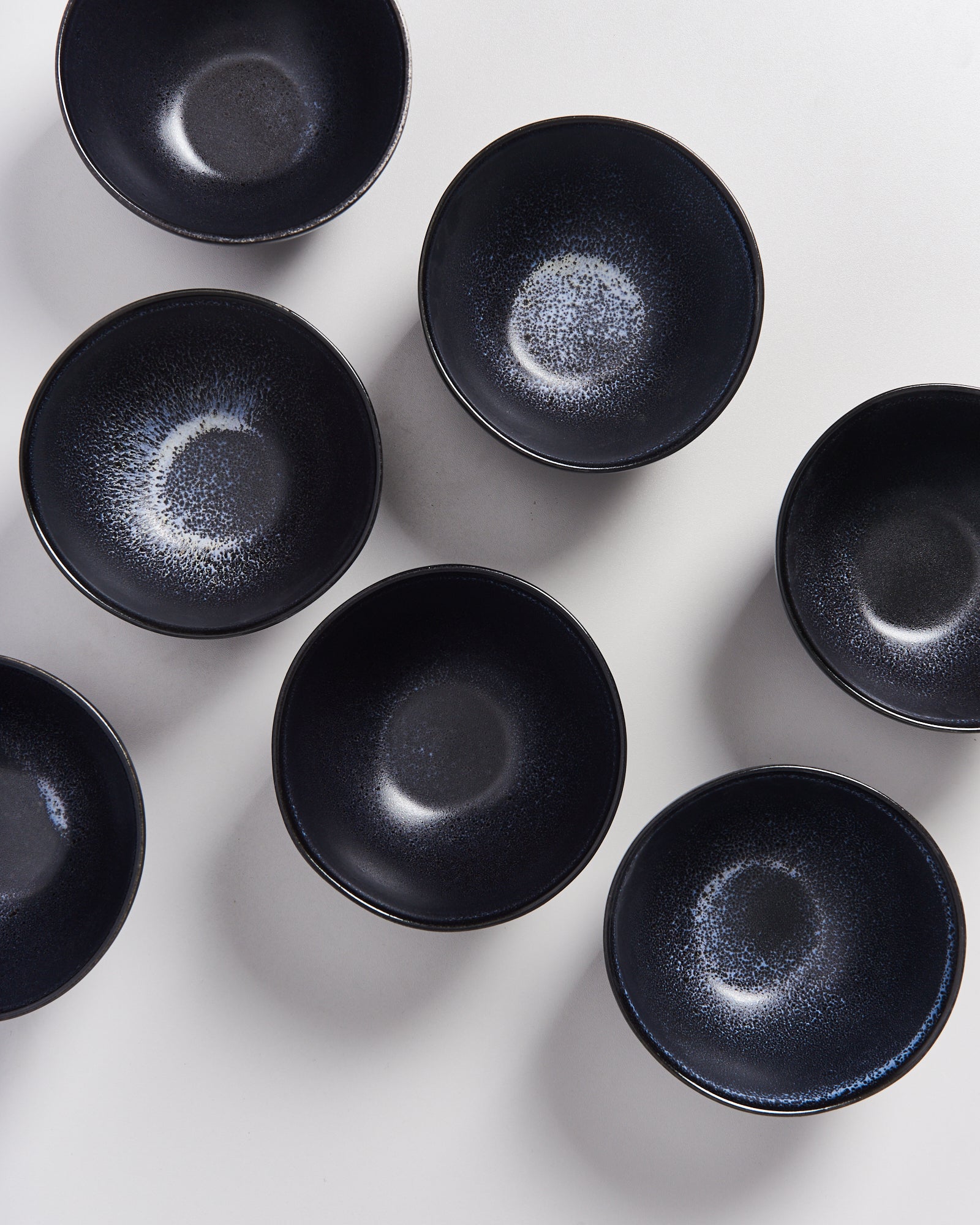 Sieben schwarze Schalen mit blauen Mustern stehen auf einer weißen Oberfläche.